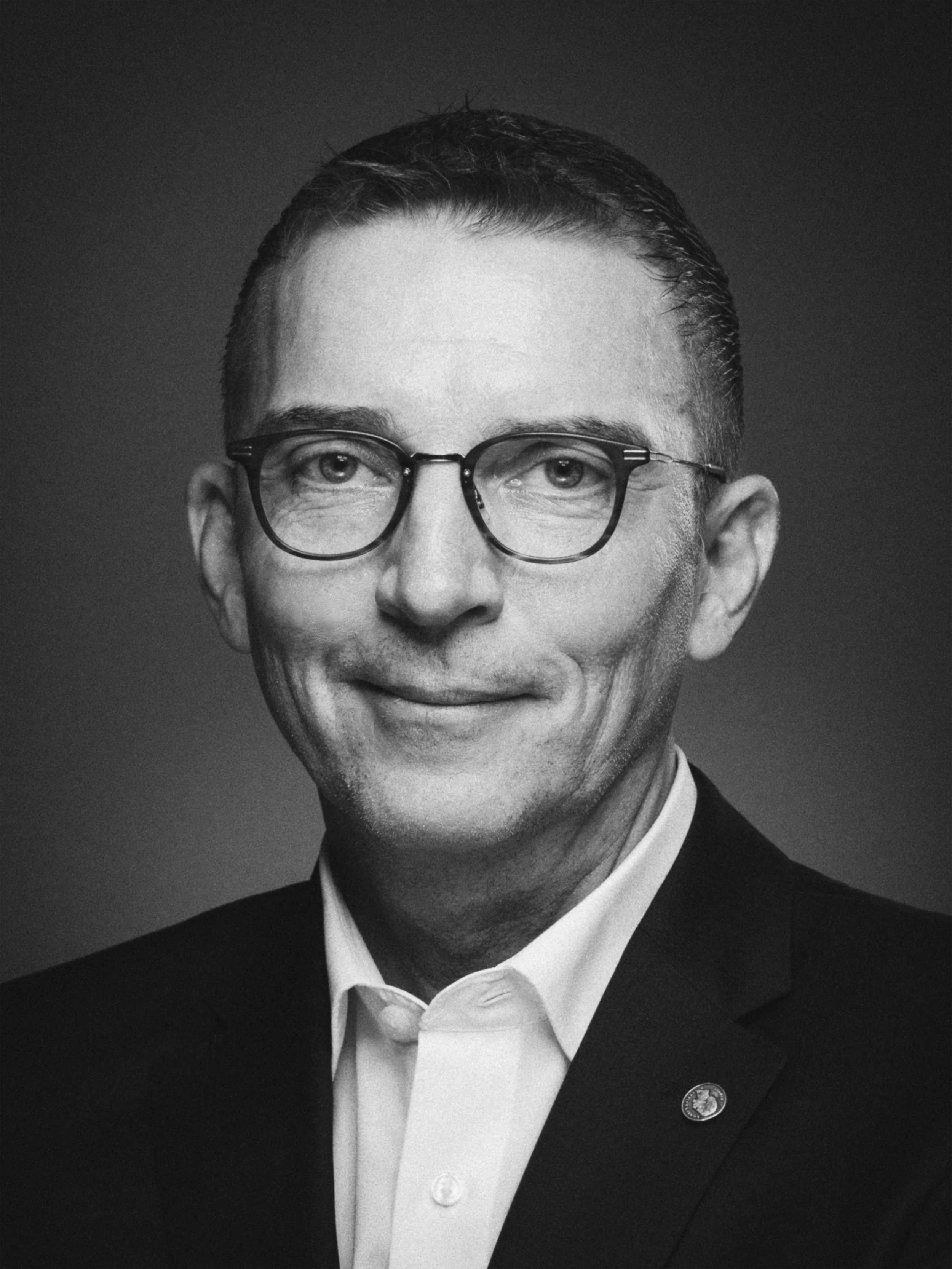 Schwarz-weiß Porträt eines Mannes mit Brille und Anzug, der in die Kamera lächelt.