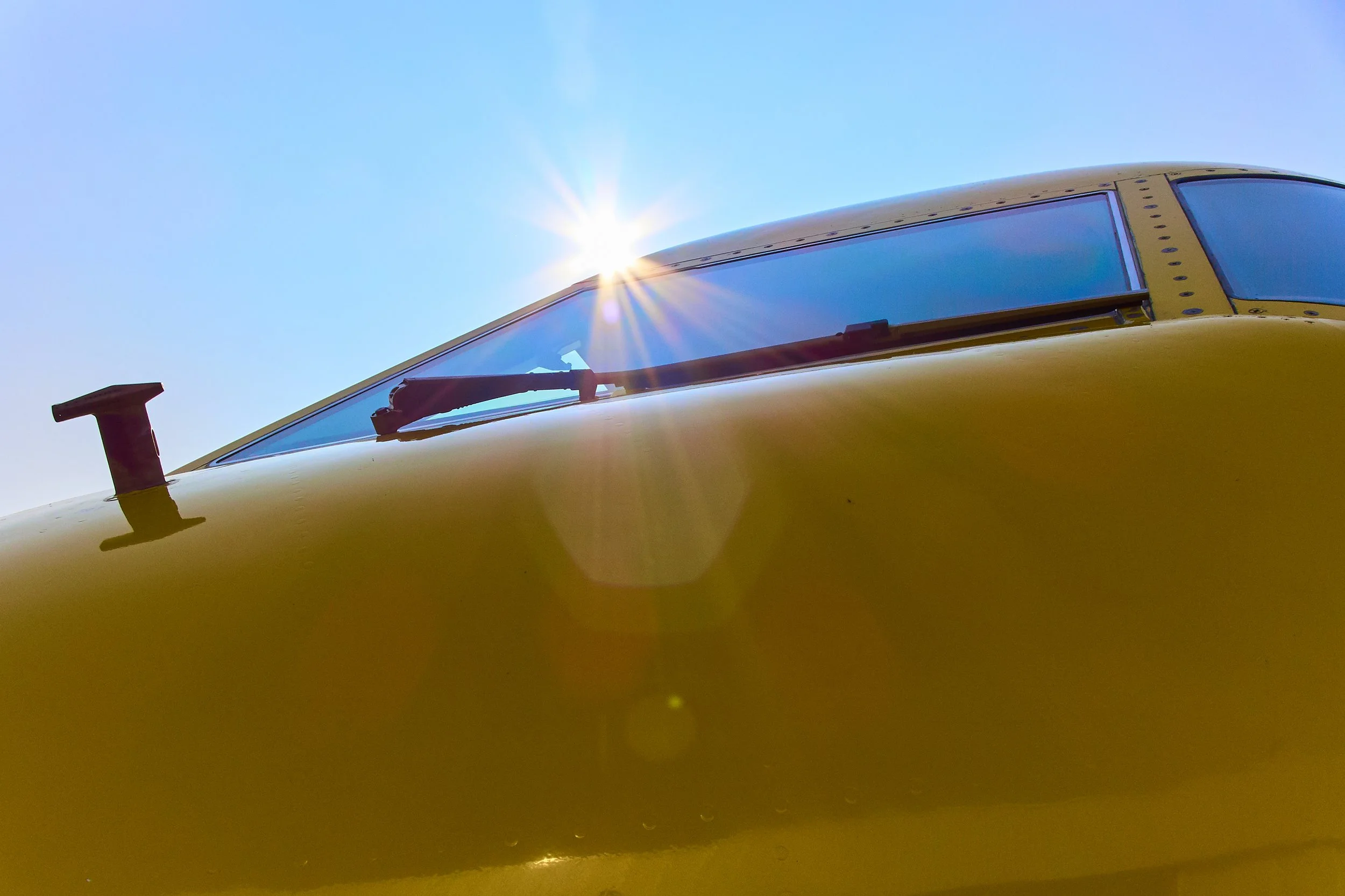 Blick auf die vordere Flugzeugkabine, gelb lackierte Oberfläche, Sonnenlichtreflexionen, Flugzeugfenster, Windschutzscheibe, Wischer, Teil des Cockpits.