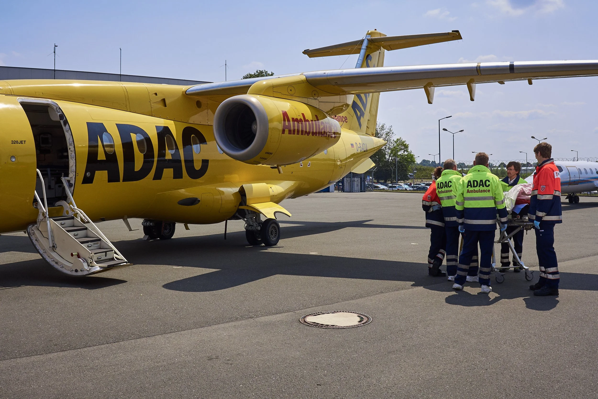 Eine gelbe Notfallmaschine auf einem Flugfeld, auf der Notfallpersonal eine verletzte Person auf eine Trage legt, während sie bereit sind, sie zu transportieren.