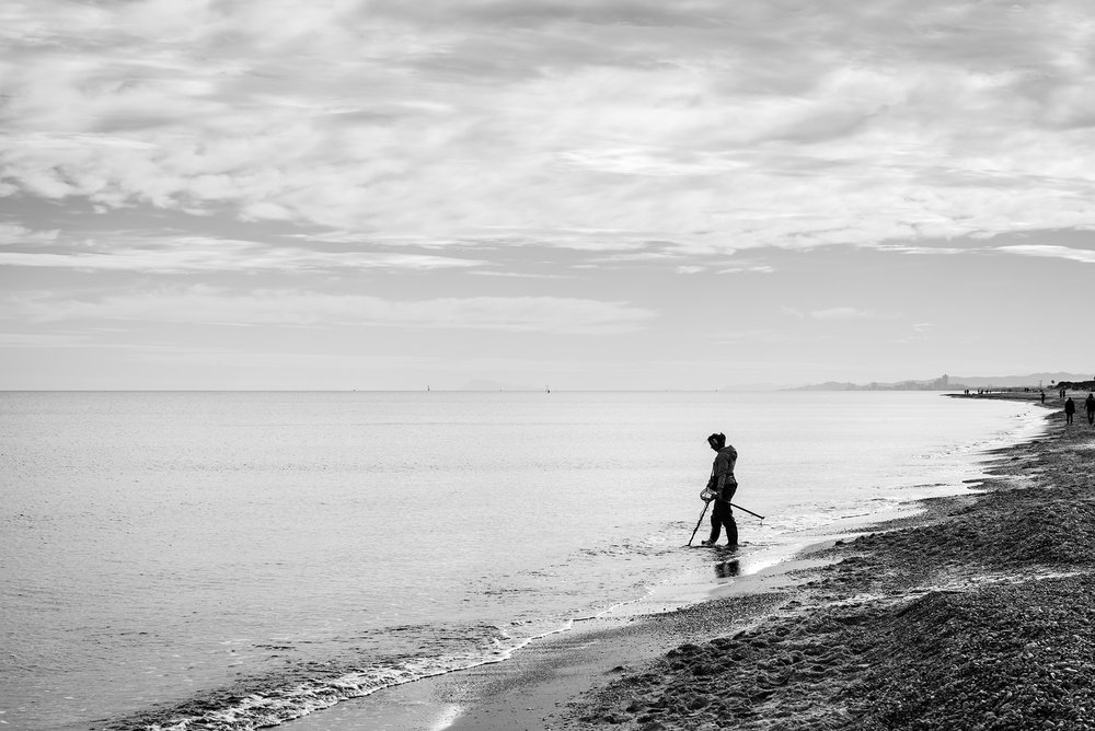 Silhouette of a female treasure hunter with a metal detector on a beach in the Mediterranean sea