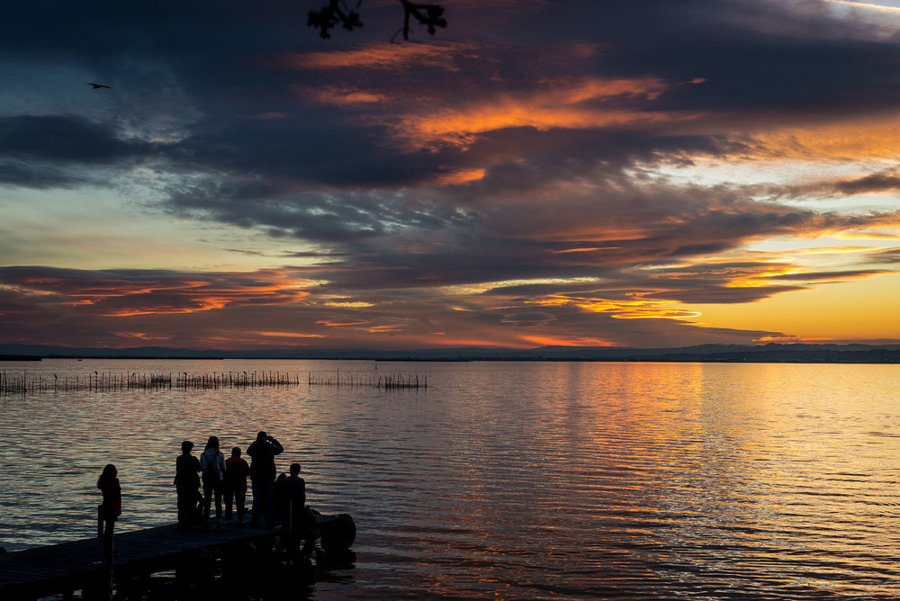 Silhouette of a small wooden jetty and tourists taking pictures at dusk in the Albufera