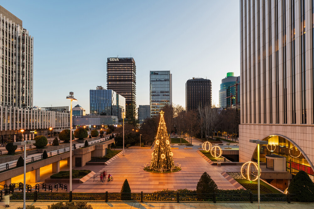 Wide-angle view of the AZCA business and financial district in Madrid with the traditional illuminated Christmas tree rising in its center.