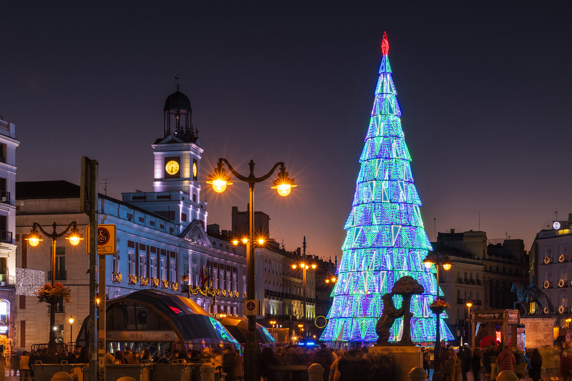 Crowds of people gather at the Puerta del Sol square in Madrid, Spain, with the traditional illuminated Christmas tree rising in its center.