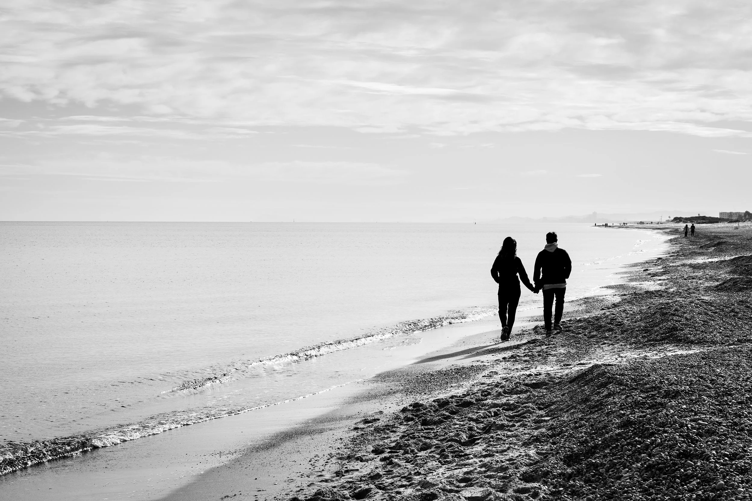 Silhouette of a couple holding hands while walking along the shore of the Mediterranean sea. Black and white.