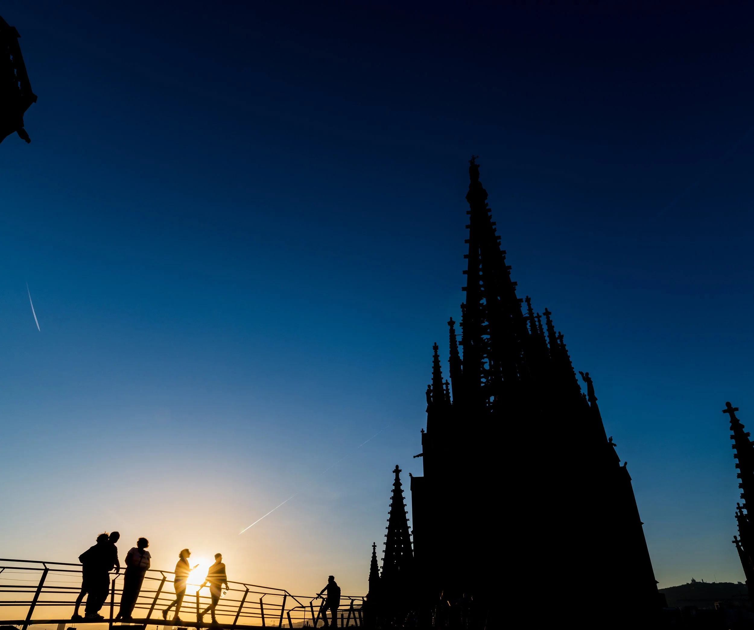 Silhouette of tourists on top of the Gothic Cathedral of Barcelona at dusk.