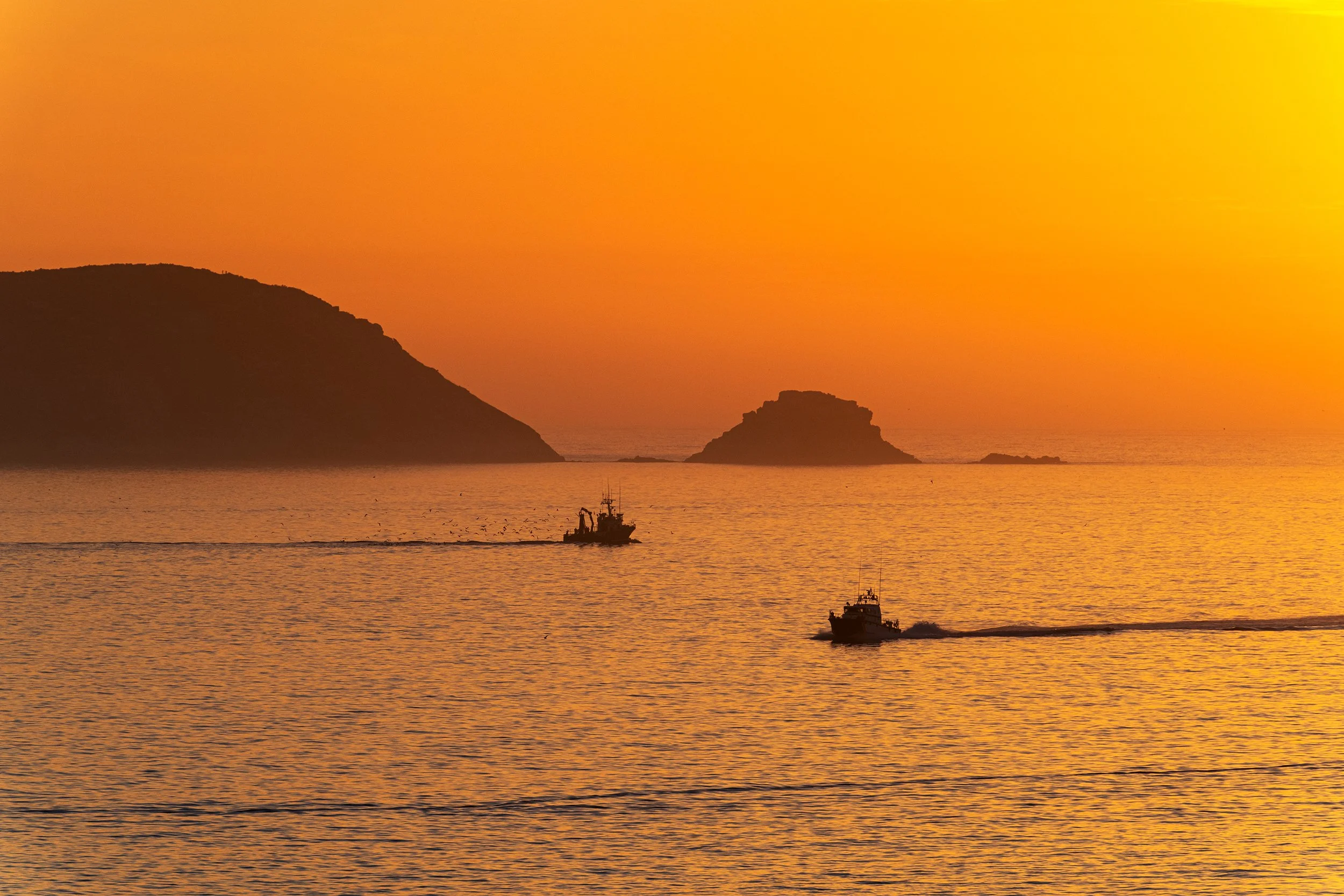 Two fishing boats sail at sunset in the Ría de Pontevedra in Galicia at dusk, with the serene Ons Islands in the background.
