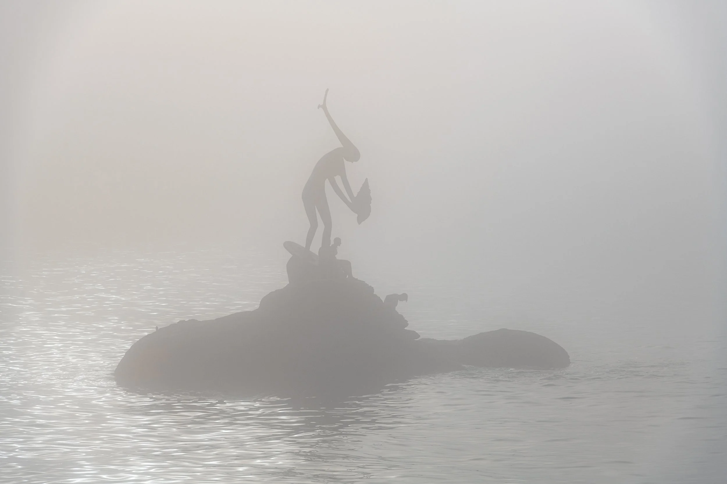 Silhouettes of bathers on top of the Madama sculpture on Silgar beach in Sanxenxo on a foggy summer day in the Rias Baixas in Galicia