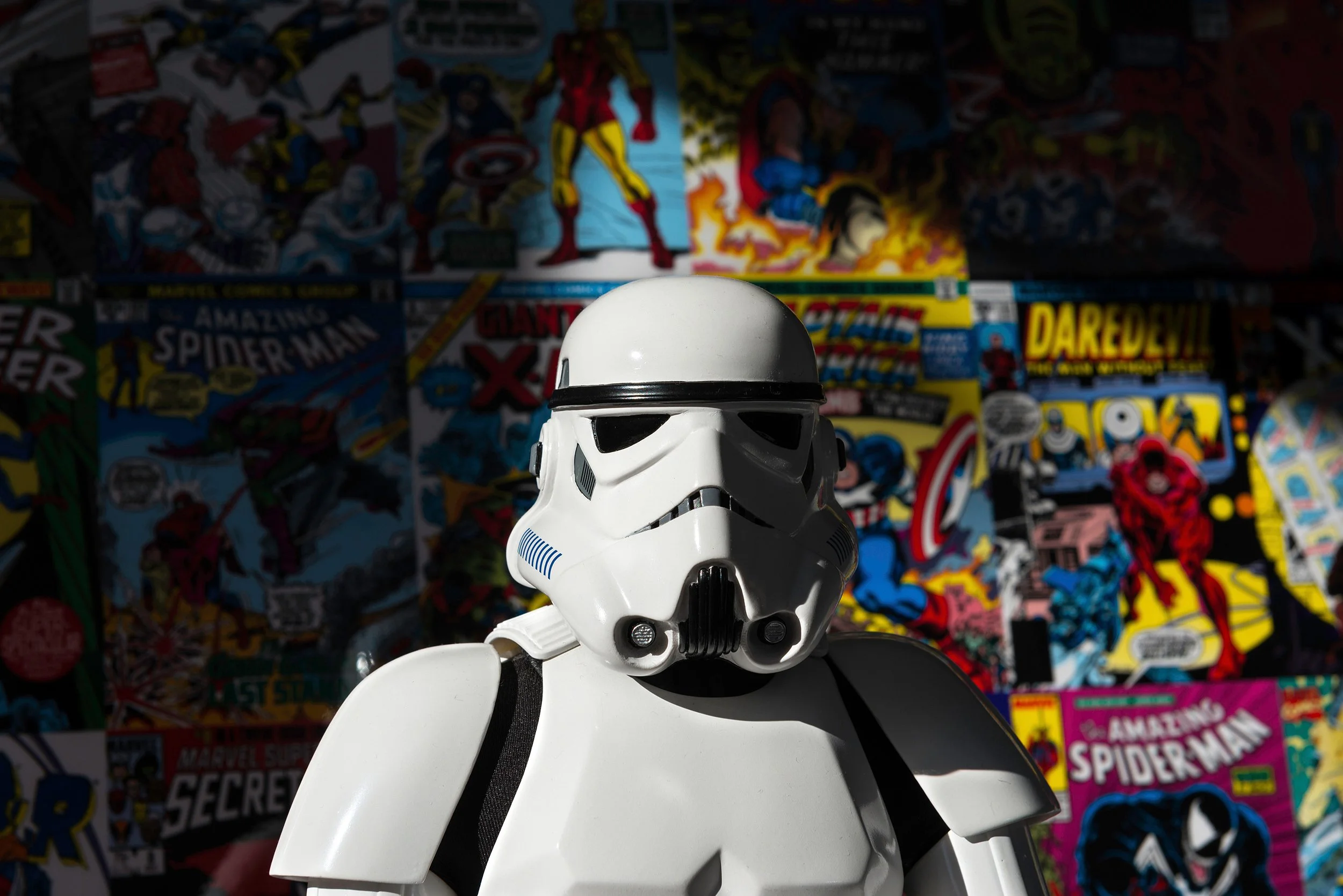 Head shot of a white Imperial Stormtrooper action figure against a colorful wall, covered with old Marvel Super-heroes comic books 