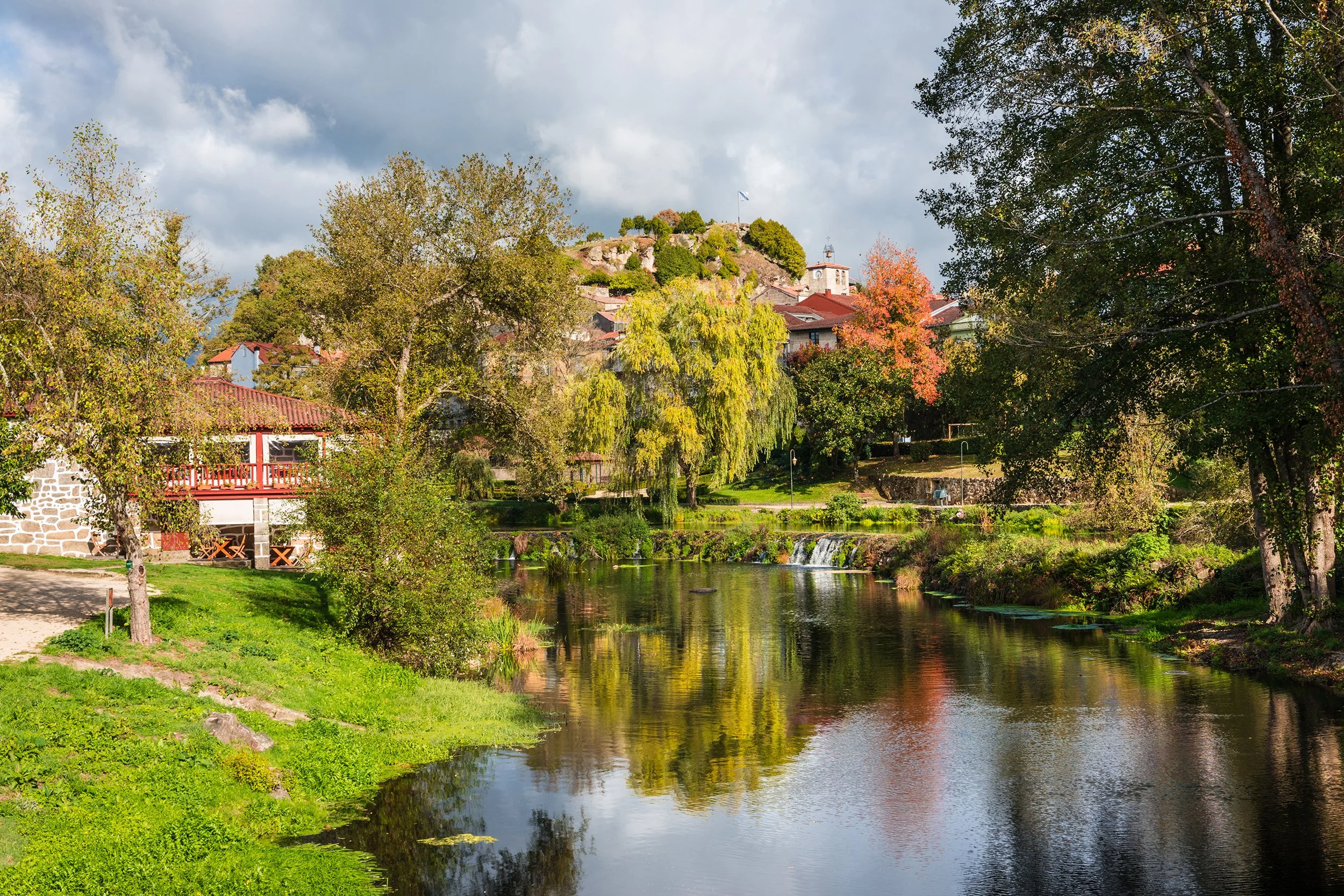 Fall foliage and medieval Roman bridge reflected on the water in the Galician village of Allariz, Ourense.