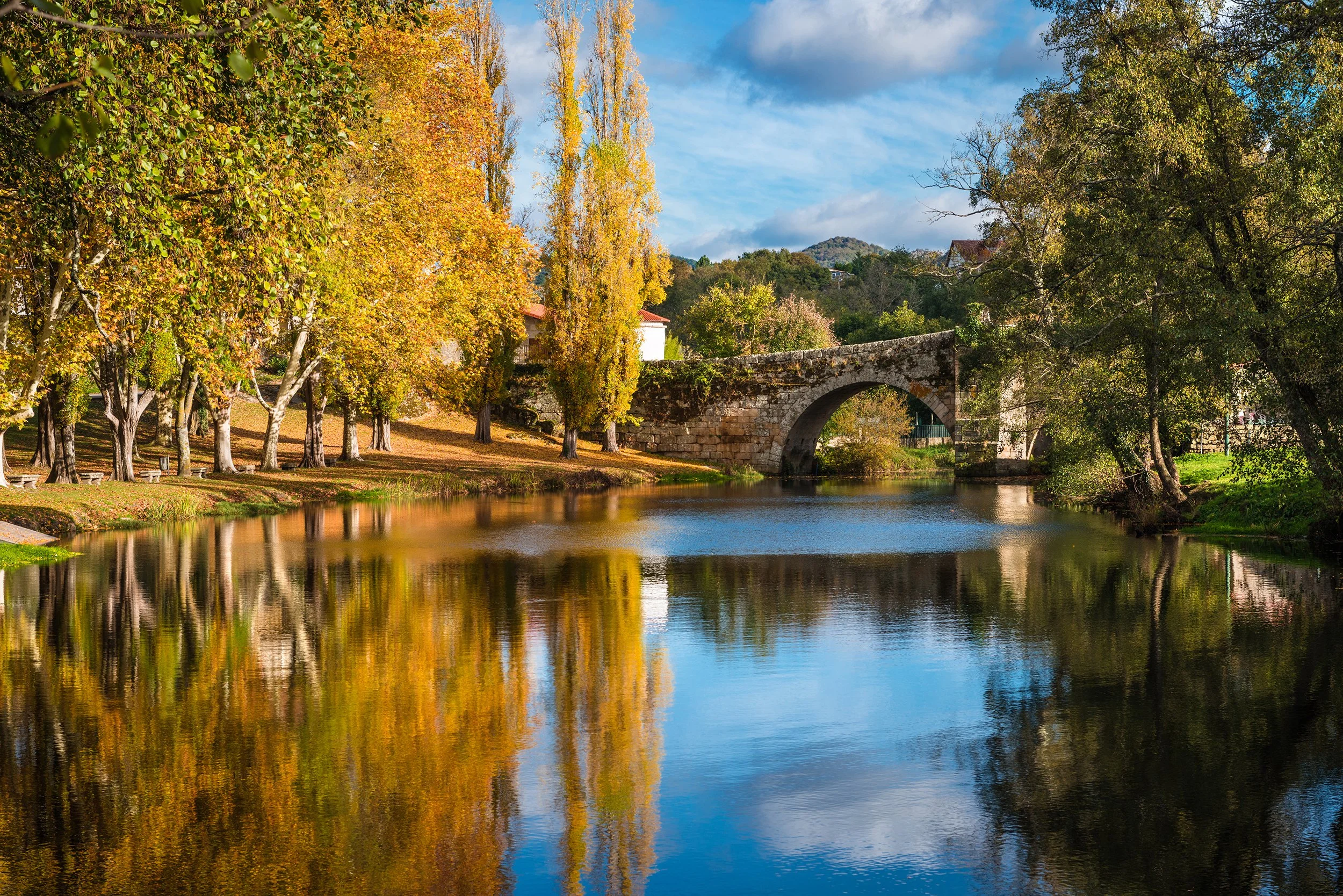 Fall foliage and medieval Roman bridge reflected on the water in the Galician village of Allariz, Ourense.