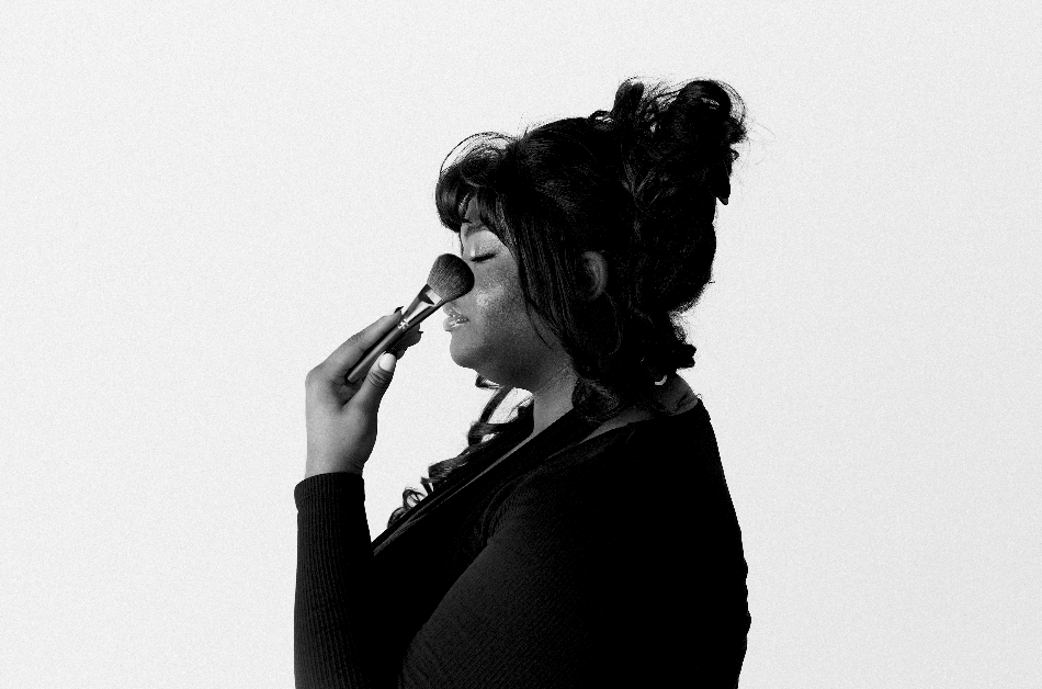 Black and white image of a woman applying makeup with a brush, side profile view.