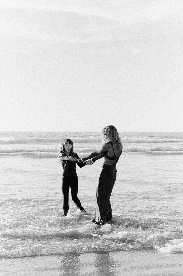 A woman and a young girl holding hands while standing in the ocean waves at the beach.