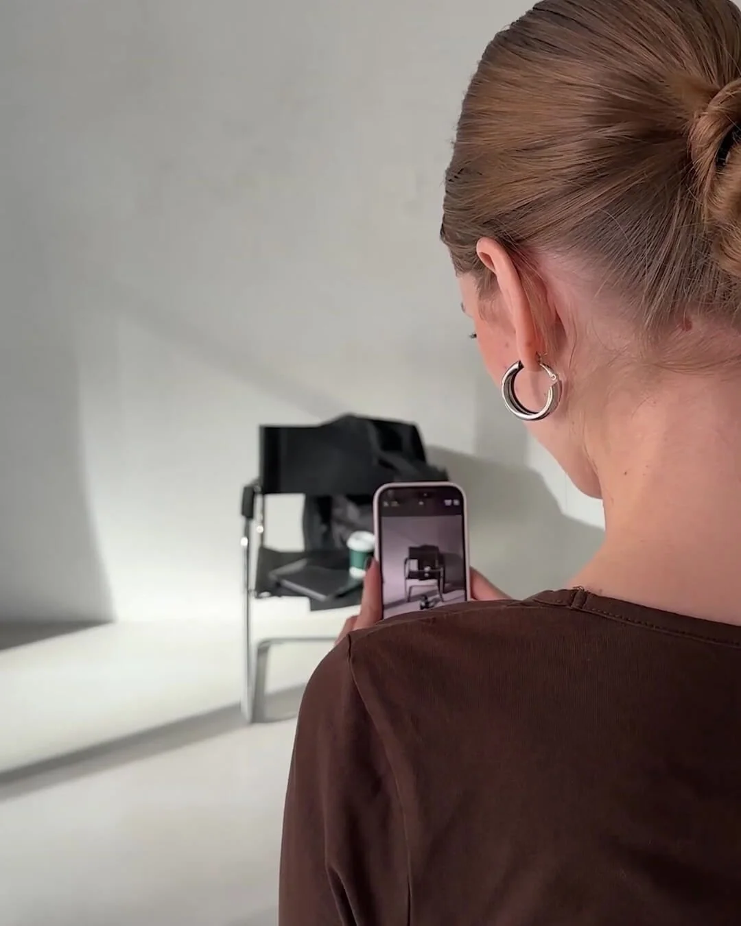 A woman with blonde hair in a bun taking a photo with her smartphone of an art installation in a gallery.