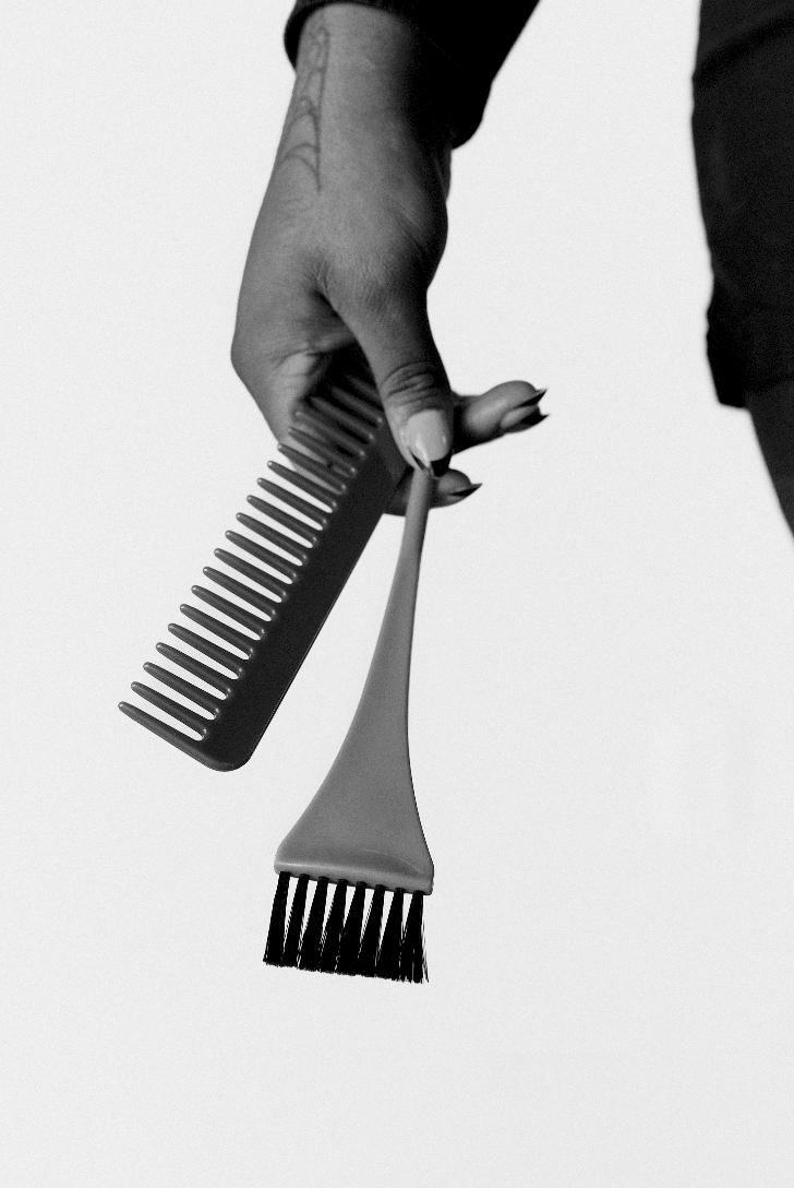 Black and white image of a hand holding a comb and a hair dye brush.