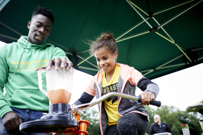  Girl wearing yellow tshirt on stationary bike with man wearing green hoodie standing next to her 