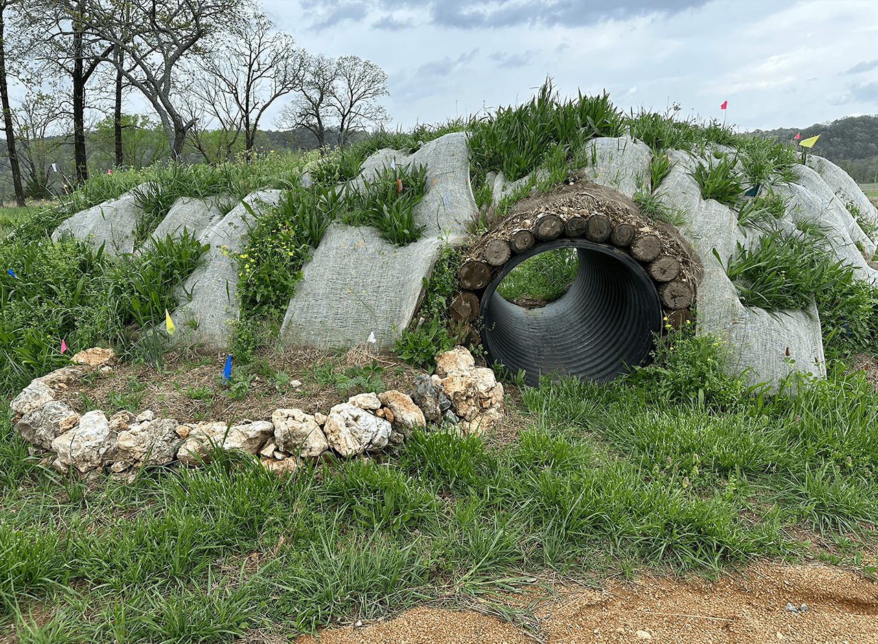 A large hugelkultur mound with a culvert going through the center and a rock stack garden bed with cover crops growing.