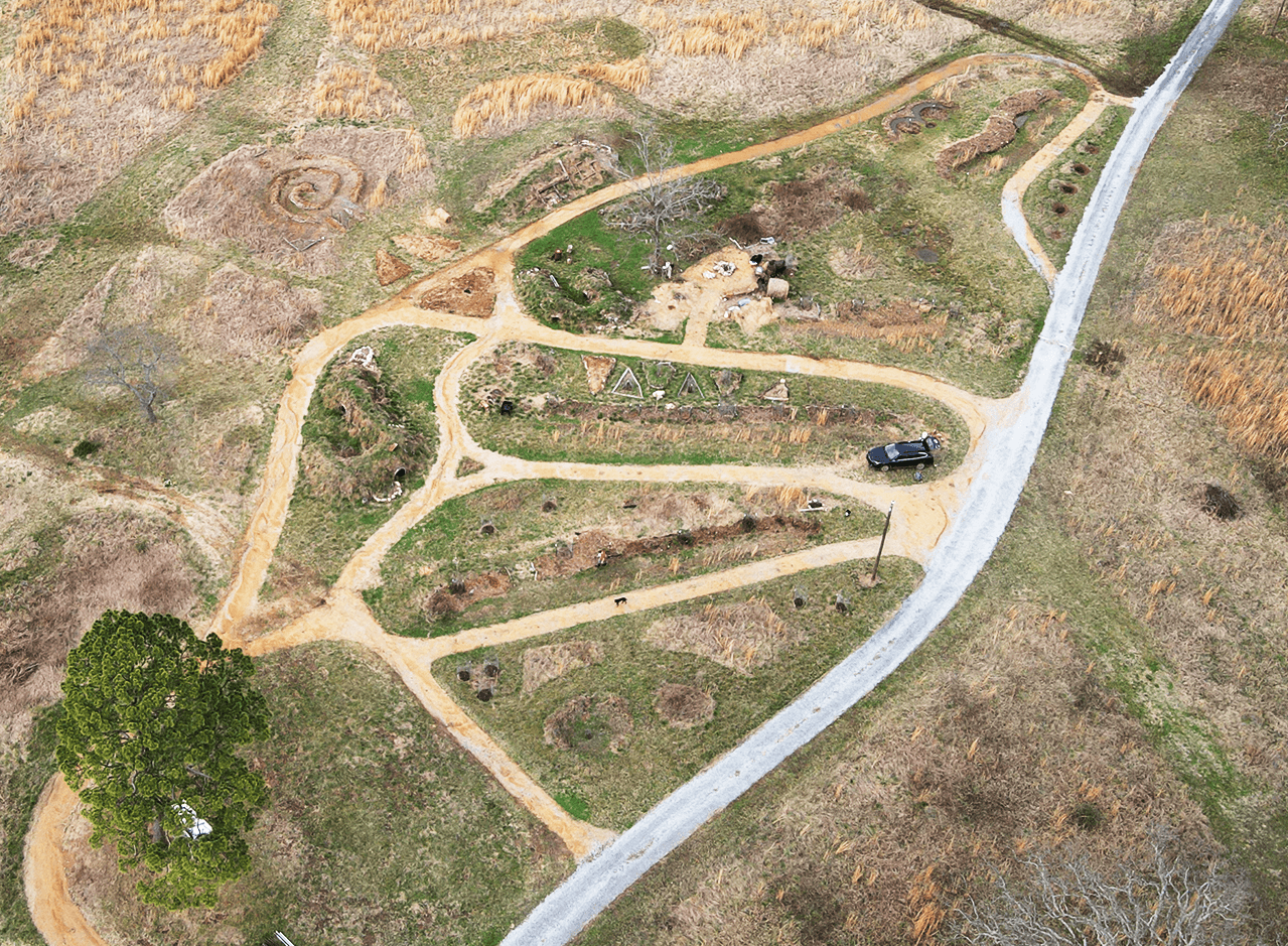An aerial image of a food forest polyculture orchard with clear pathways, swales, and other earthworks including a bee bubbler courtyard.