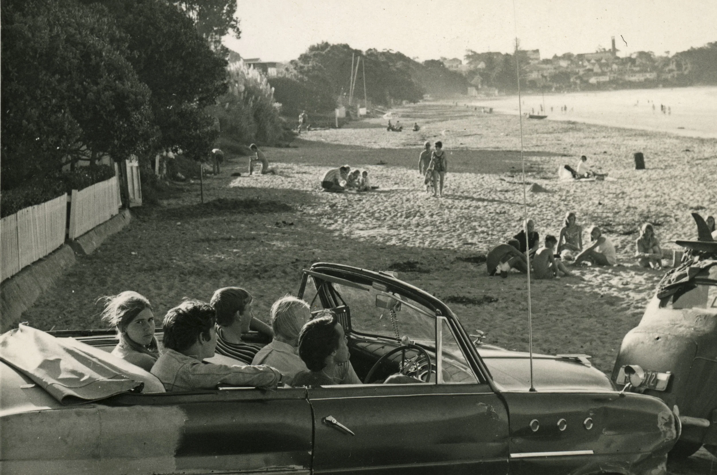 A group of teenagers in a beaten up open top car at the southern end of Takapuna Beach, c. 1960s.