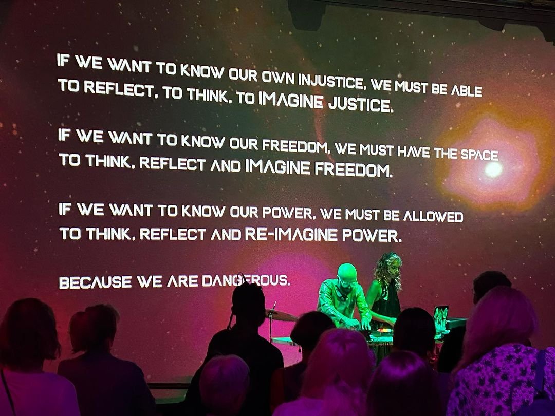  A woman and a man on stage playing music in front of giant projected image of a statement about freedom, justice and power 