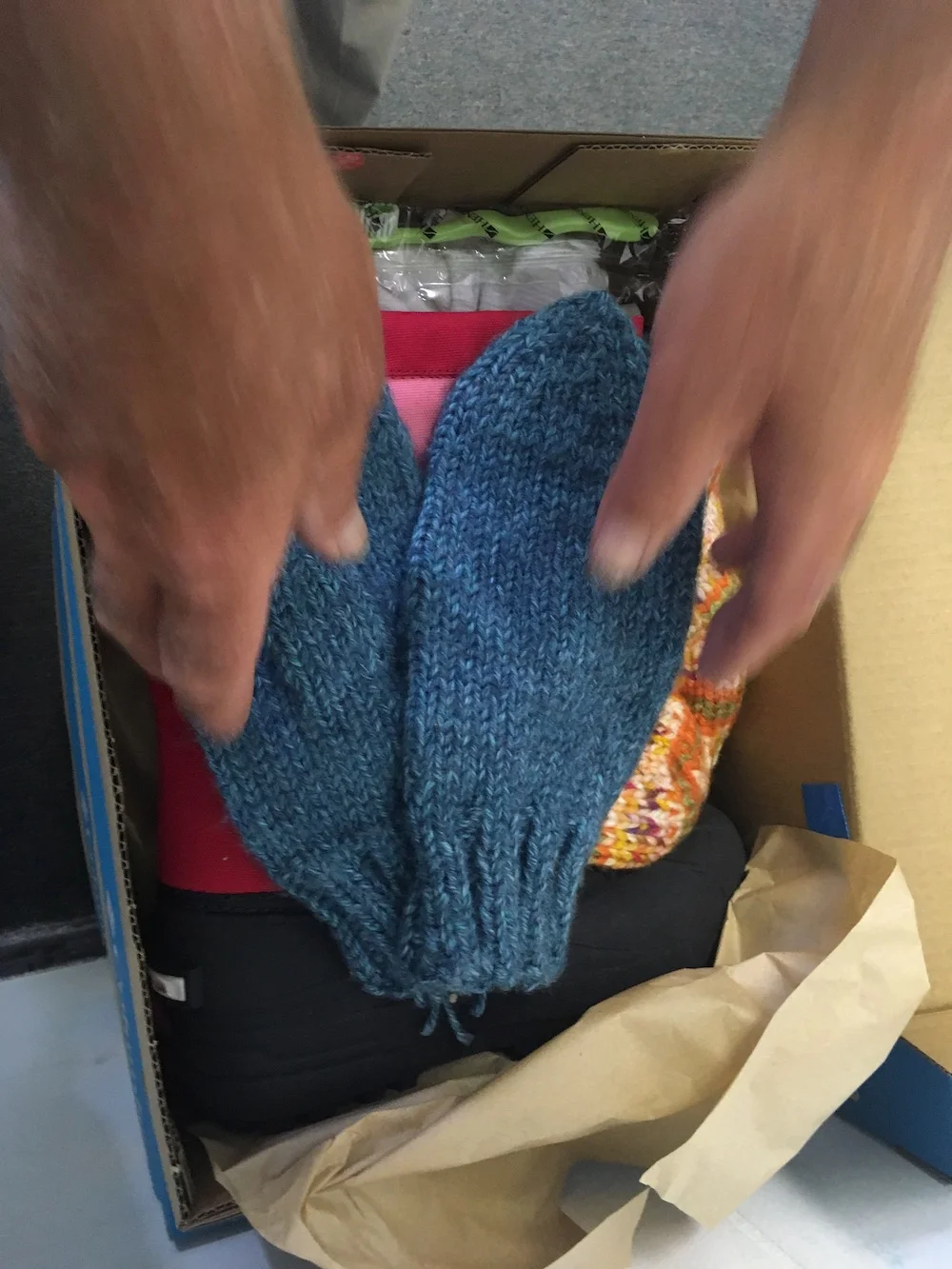 Mittens being place in a box with boots and a hat.