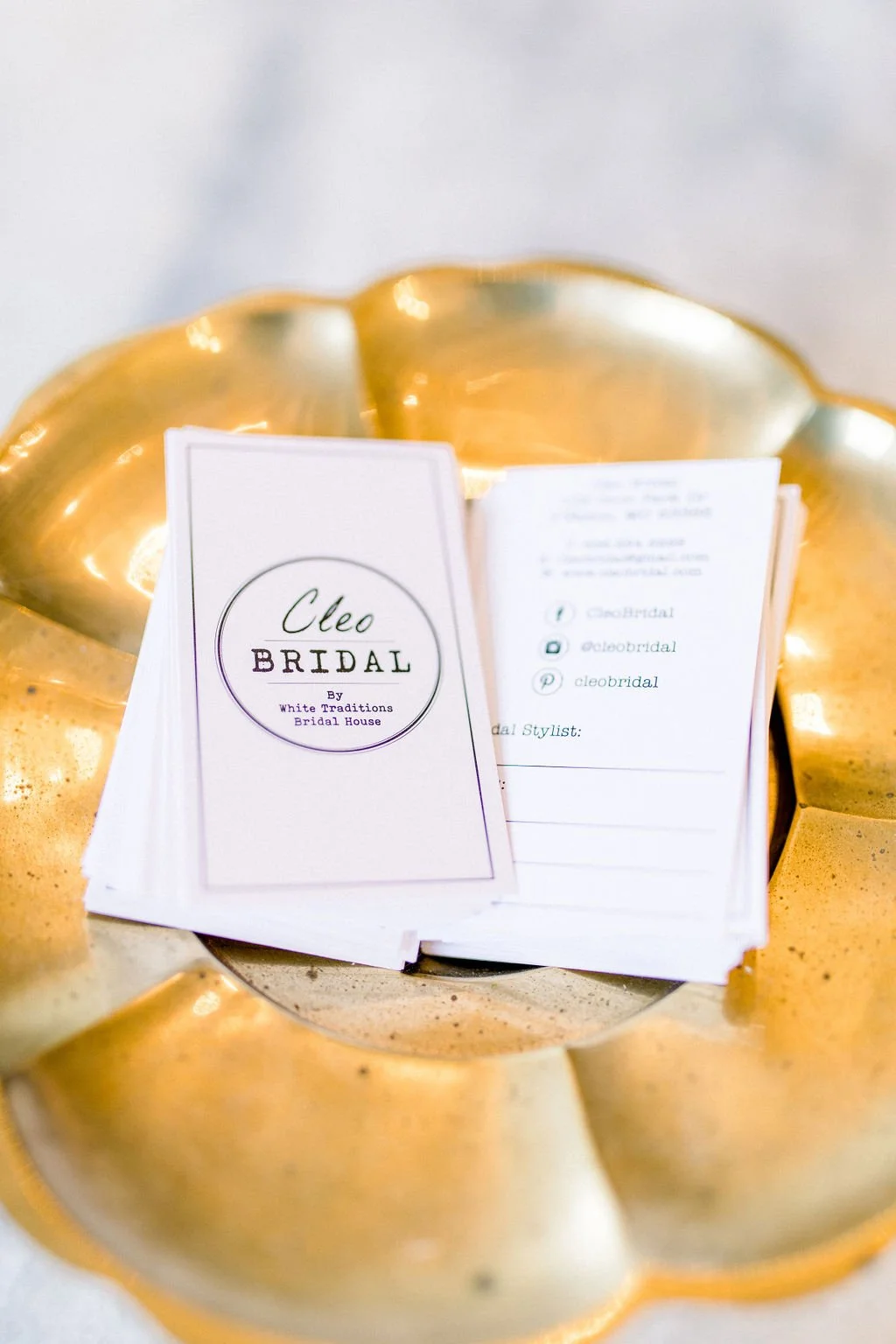 Business cards placed on a golden decorative bowl, promoting Cleo Bridal by White Traditions Bridal House.