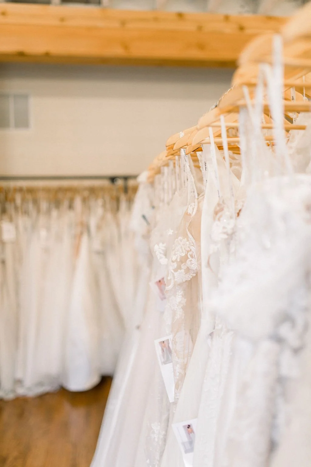 Multiple wedding dresses hanging on wooden hangers in a bridal boutique.