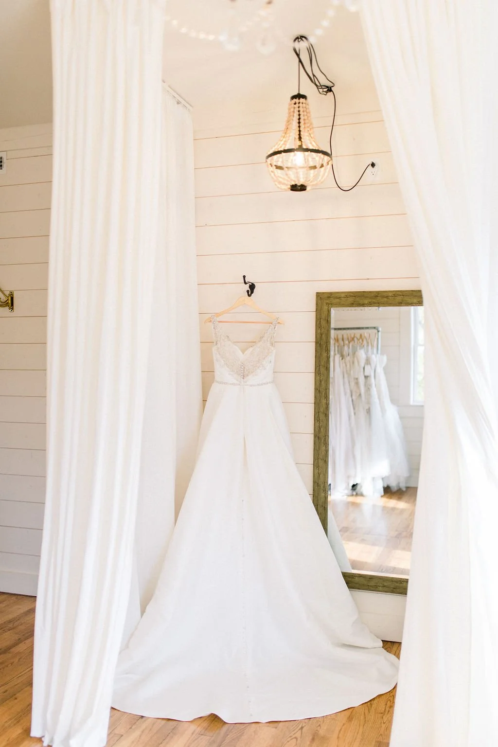 White wedding dress hanging on a wall with a mirror reflecting wedding dresses in the background.