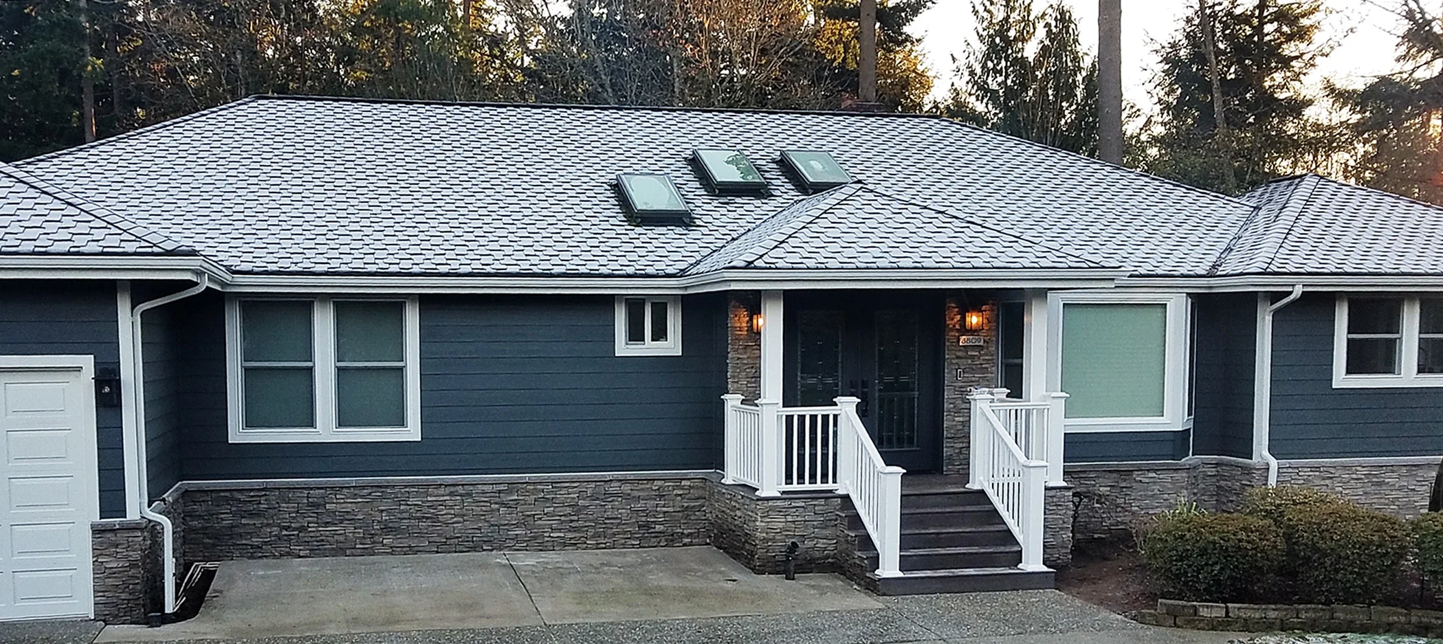Updated home exterior featuring dark blue horizontal siding, stone veneer accents, white trim, and a snow-dusted roof with skylights—part of a full exterior renovation in the Pacific Northwest.