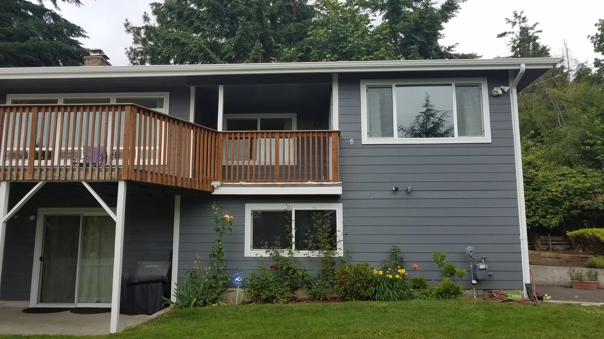 Back view of a two-story home with dark gray horizontal lap siding, white-trimmed windows, and a wood deck, highlighting a recent siding replacement and exterior renovation.