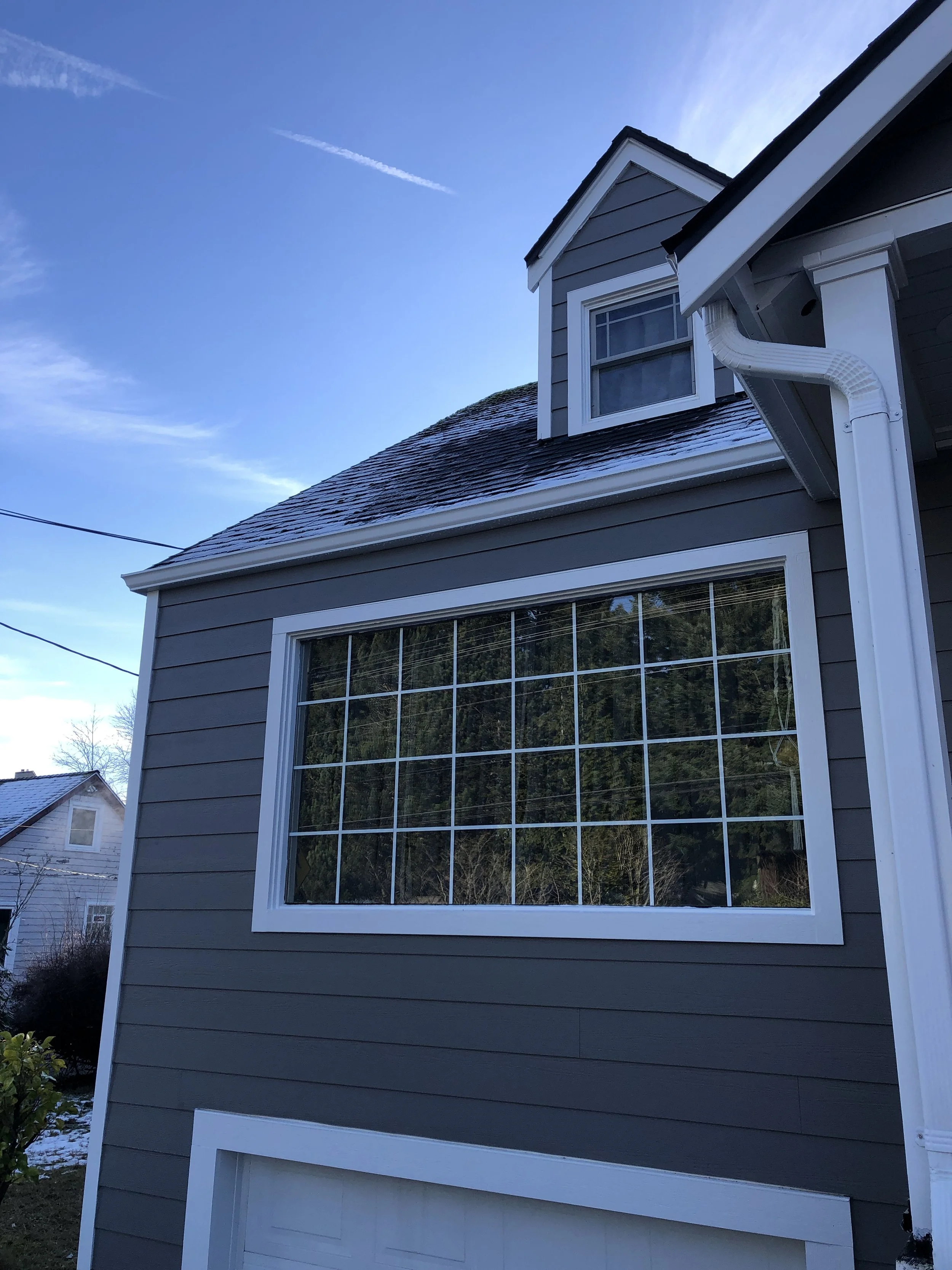 Freshly renovated home exterior with dark gray lap siding, a large grid-style window, and crisp white trim, highlighting expert siding and window replacement services.
