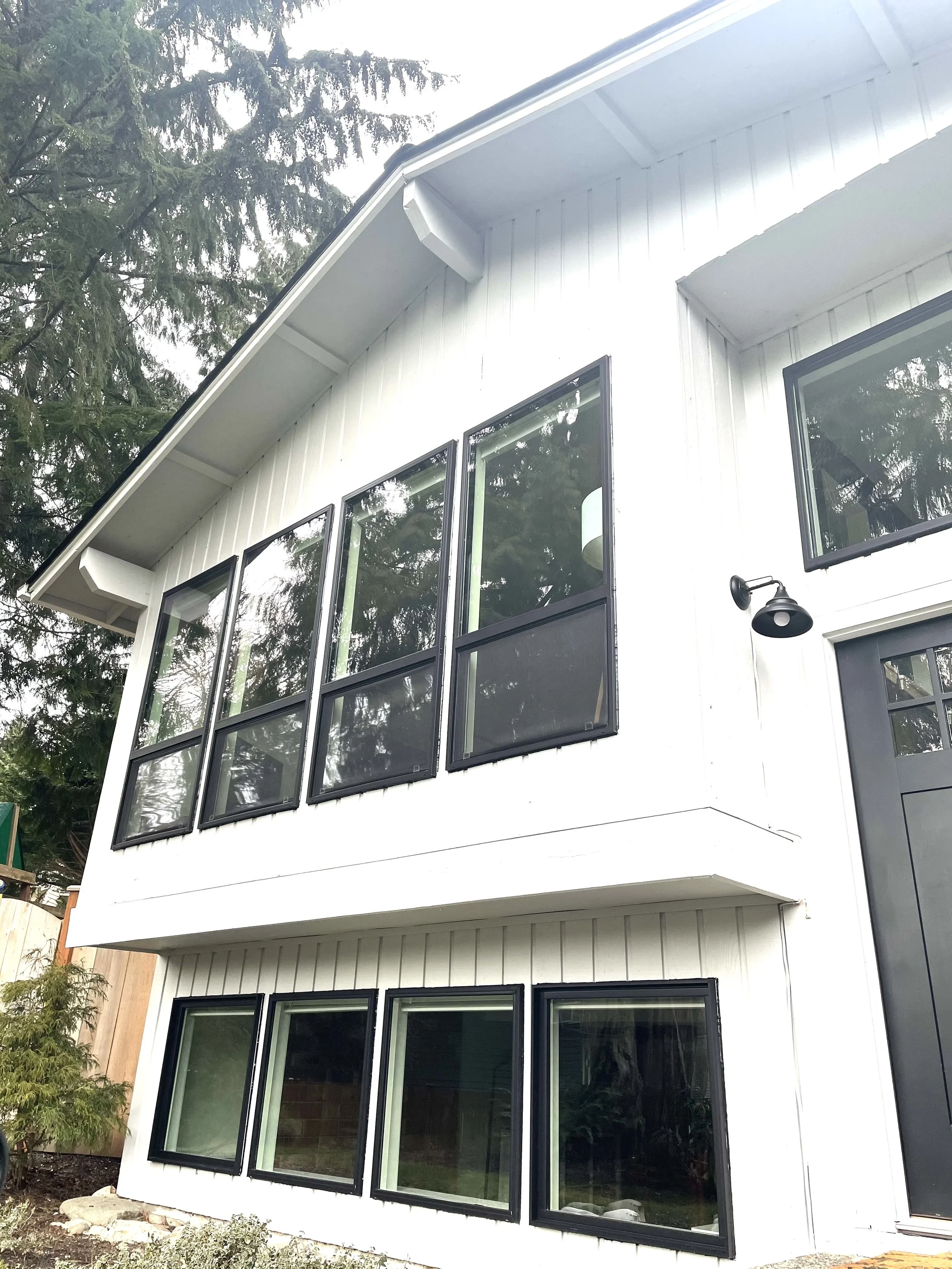 Modern home exterior with white vertical board and batten siding and large black-framed windows, showcasing a clean, contemporary look and expert siding installation.