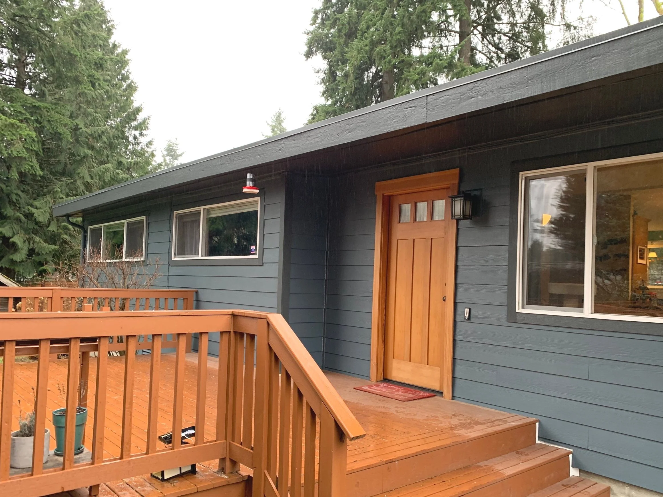 Contemporary home exterior featuring dark blue lap siding, a natural wood front door, and a custom-built stained wood deck, highlighting expert siding and entryway renovation.