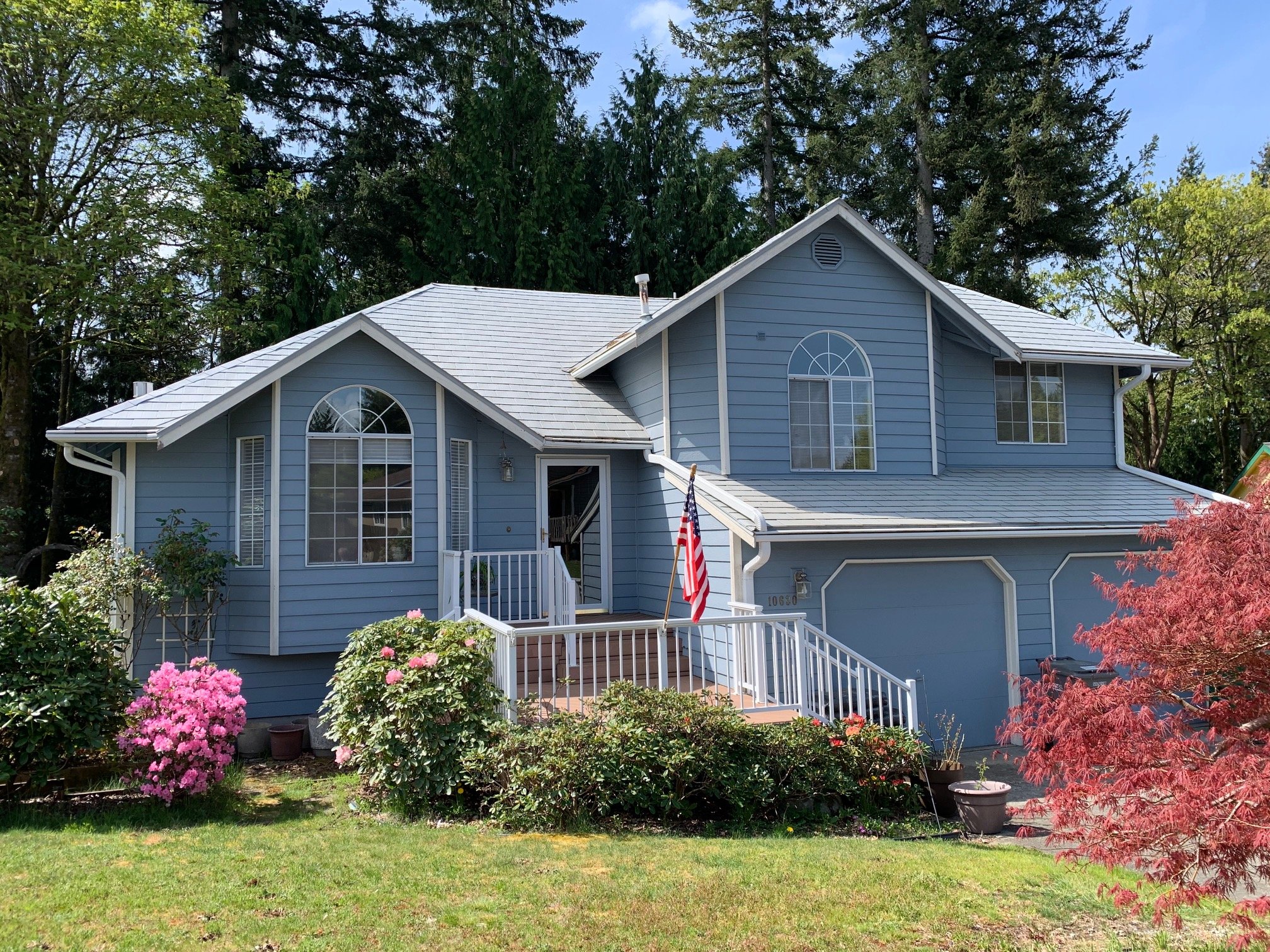 Beautiful two-story home with light blue lap siding, white trim, arched windows, and a front porch with railing—showcasing a full siding replacement and curb appeal enhancement.