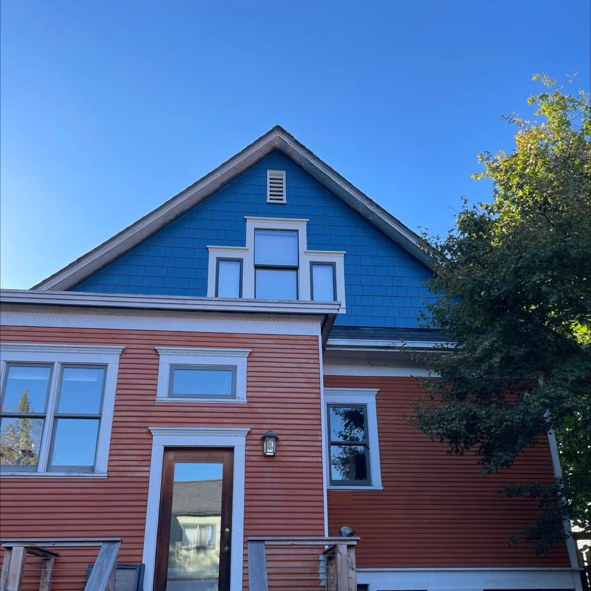 Colorful two-story home with orange lap siding, blue shingle gable, and white trim, showcasing a vibrant and well-maintained exterior renovation with historic architectural charm.