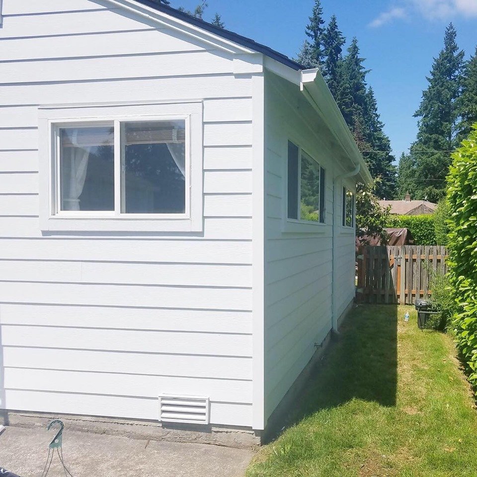 Side view of a single-story home with bright white horizontal lap siding and white-trimmed windows, illustrating a clean and modern siding replacement in a suburban setting.