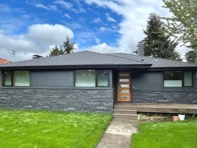 Modern single-story home with dark stone veneer and horizontal siding, featuring black-framed windows and a contemporary wood and glass front door—highlighting a sleek exterior remodel.