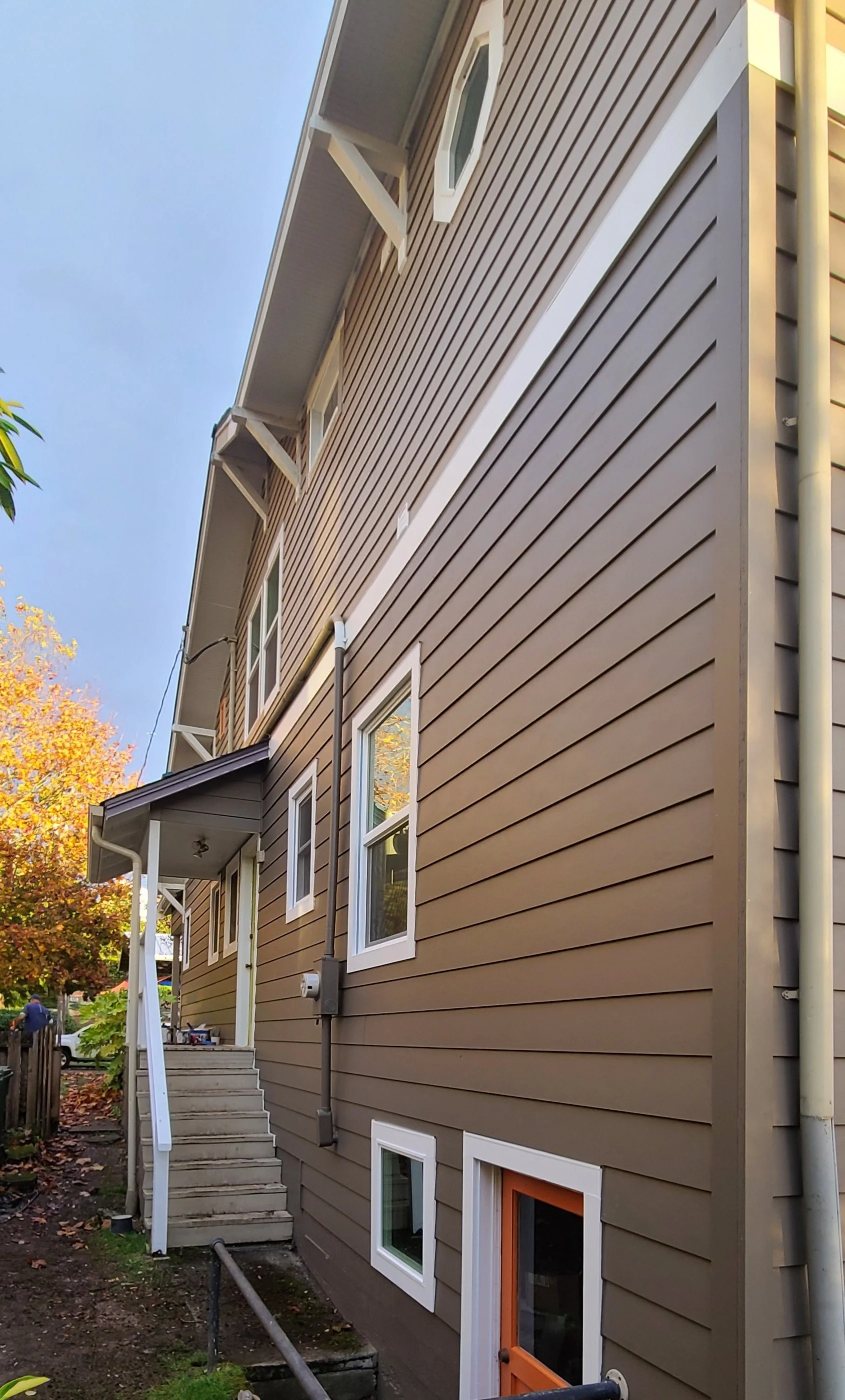 Side view of a multi-story home with fresh brown fiber cement lap siding, white window trim, and a bold orange basement door, showcasing high-quality exterior siding replacement