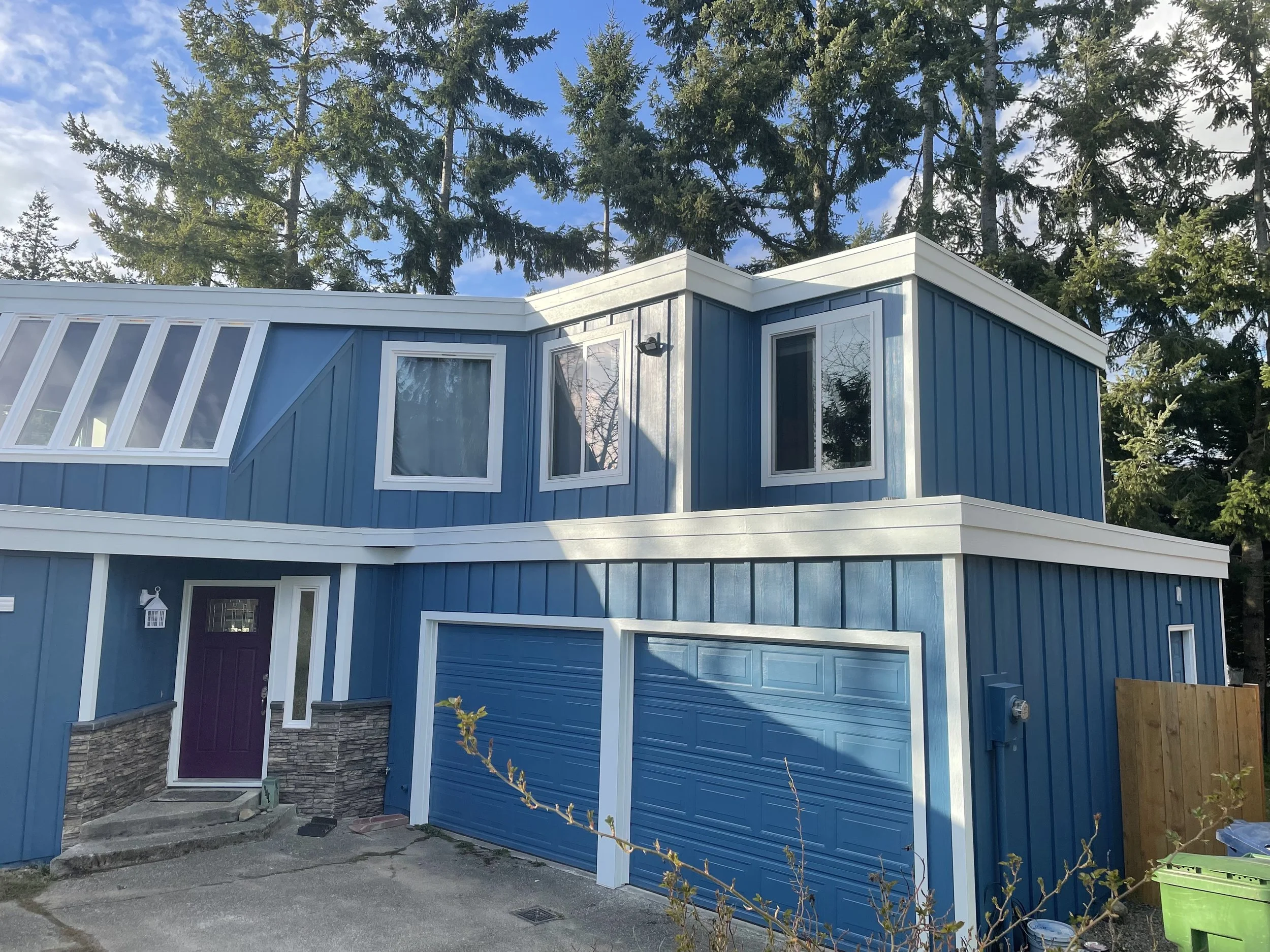 Contemporary two-story home featuring blue board and batten siding, white trim, stone accents, and a bold purple front door—highlighting a custom exterior renovation with modern architectural details.