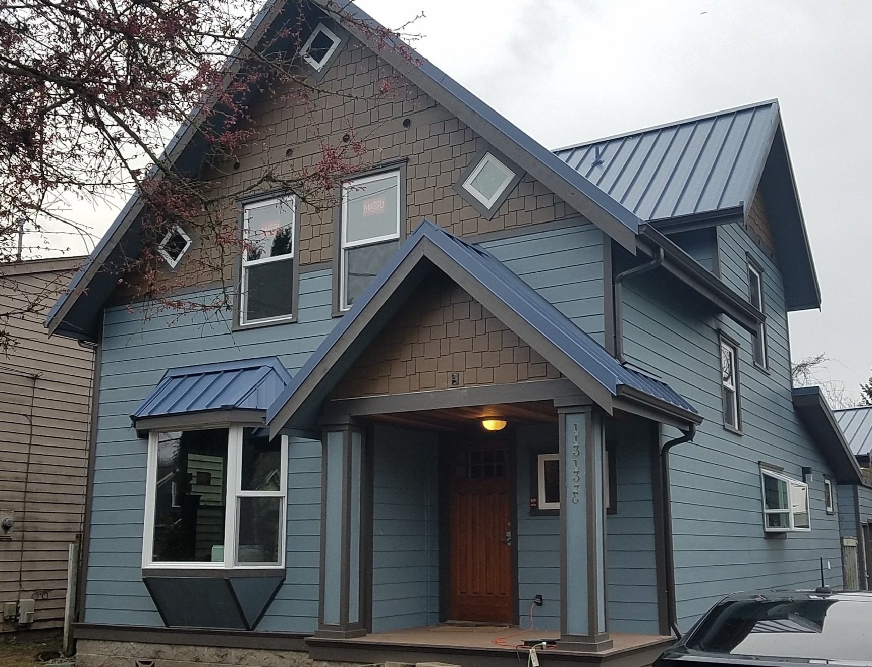 Craftsman-style home with blue horizontal lap siding, brown shake gable accents, and a metal roof, featuring unique diamond windows and detailed trim—demonstrating a customized exterior siding project.