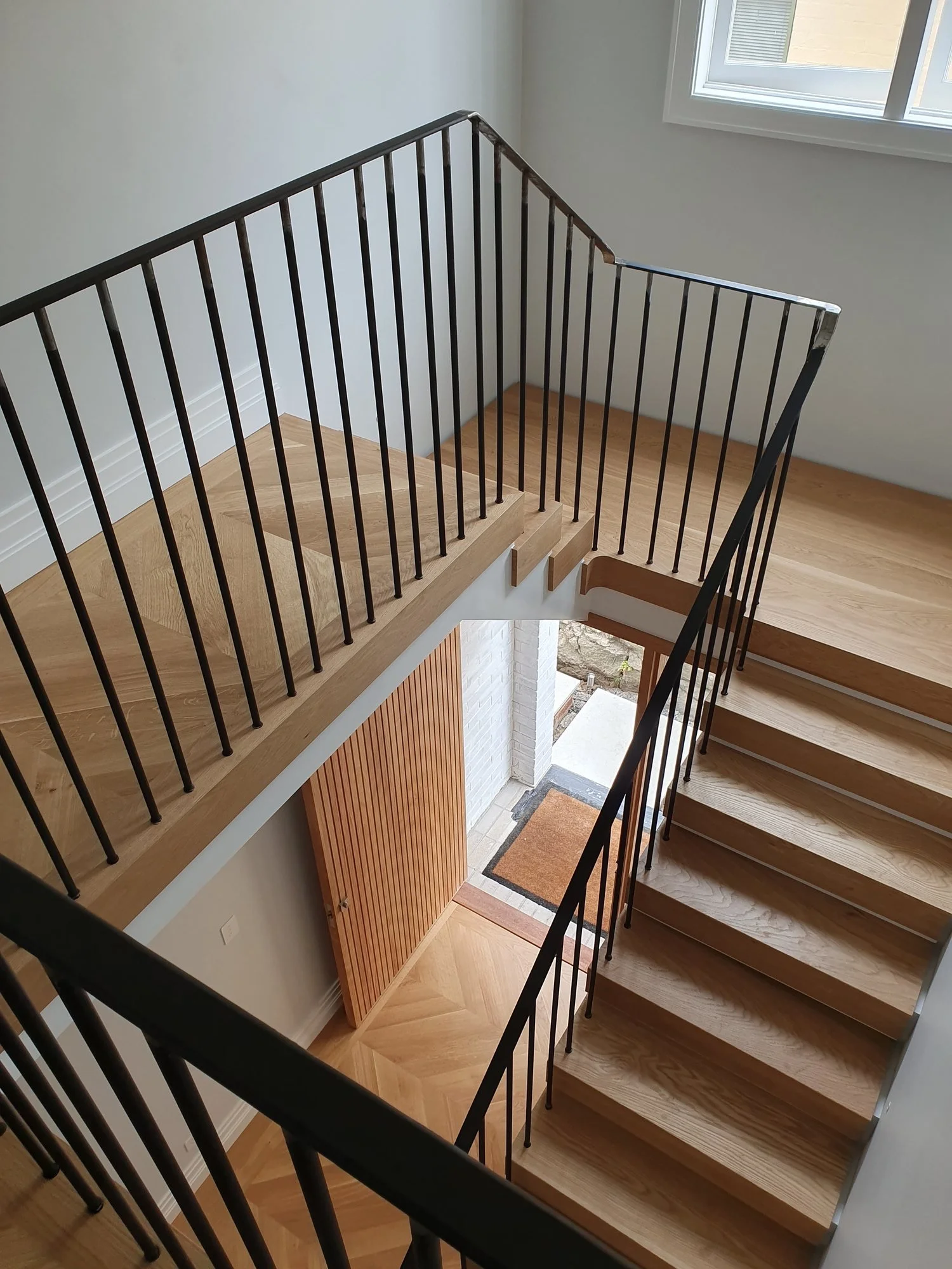  Looking down a U-shaped oak staircase with black powder-coated balustrade over a chevron oak floor, Sydney 
