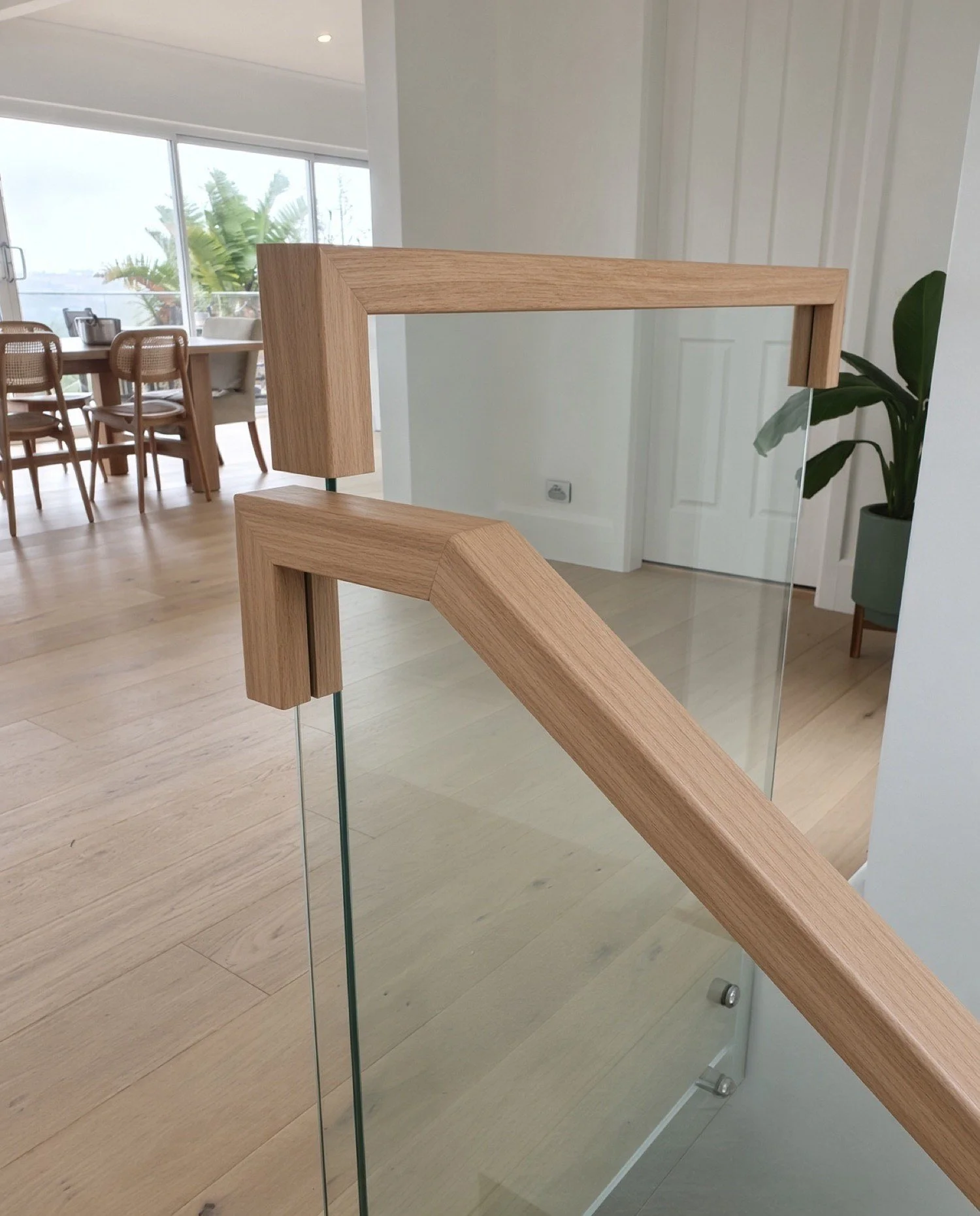  Square oak handrail mitred around a frameless glass balustrade beside an open-plan dining area, Sydney 