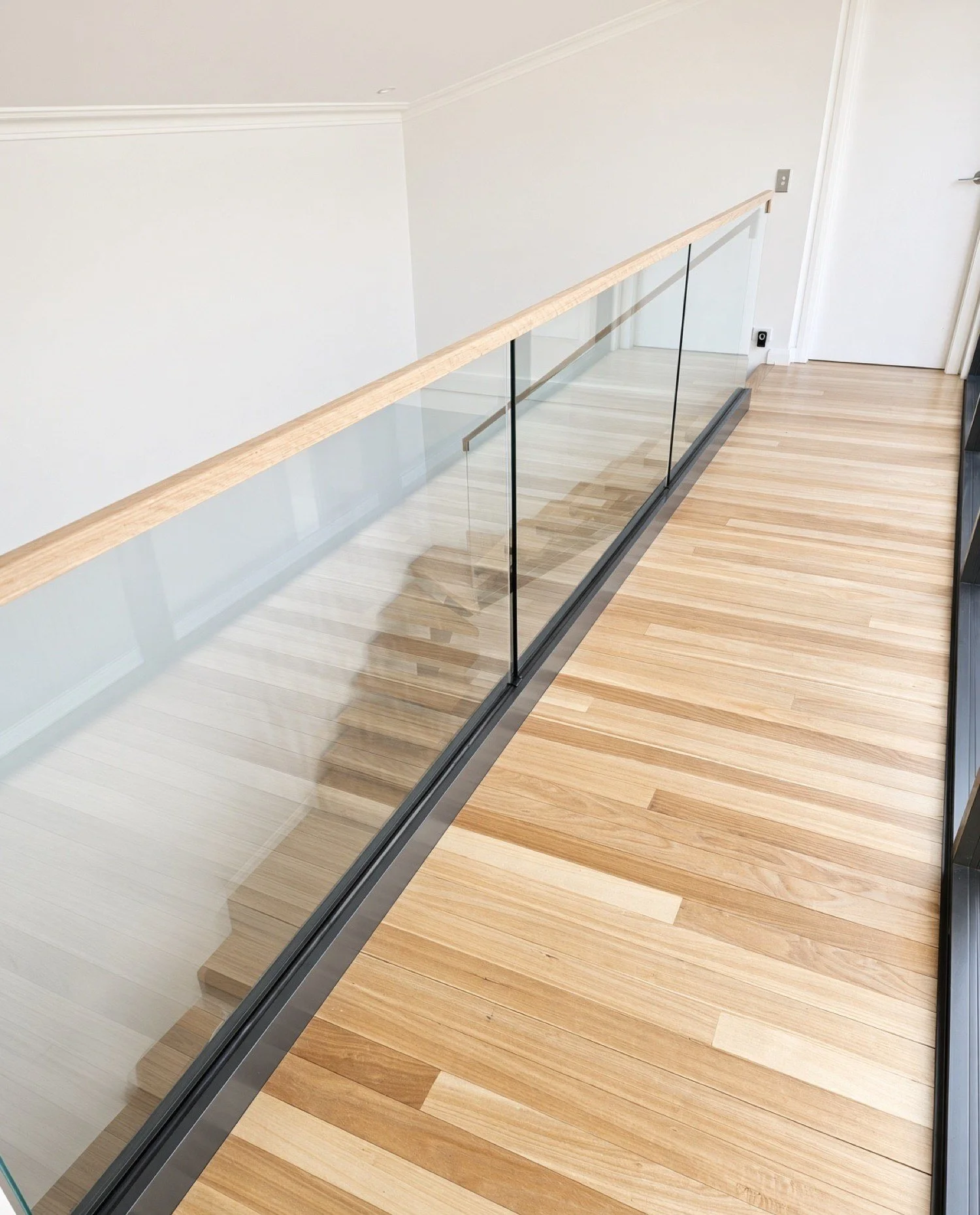  Frameless glass balustrade in a slim black channel with an oak top rail along a hardwood landing, Northern Beaches 