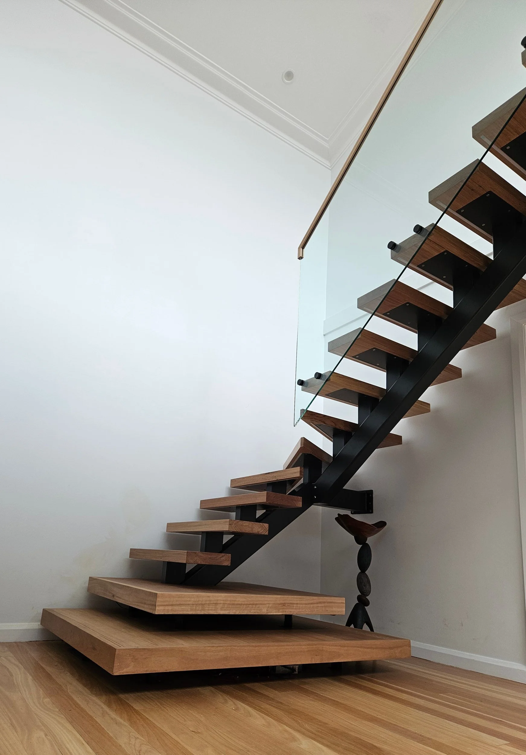 Black steel mono-stringer staircase with thick timber treads, two floating bottom landing blocks and a frameless glass balustrade with timber handrail, Sydney