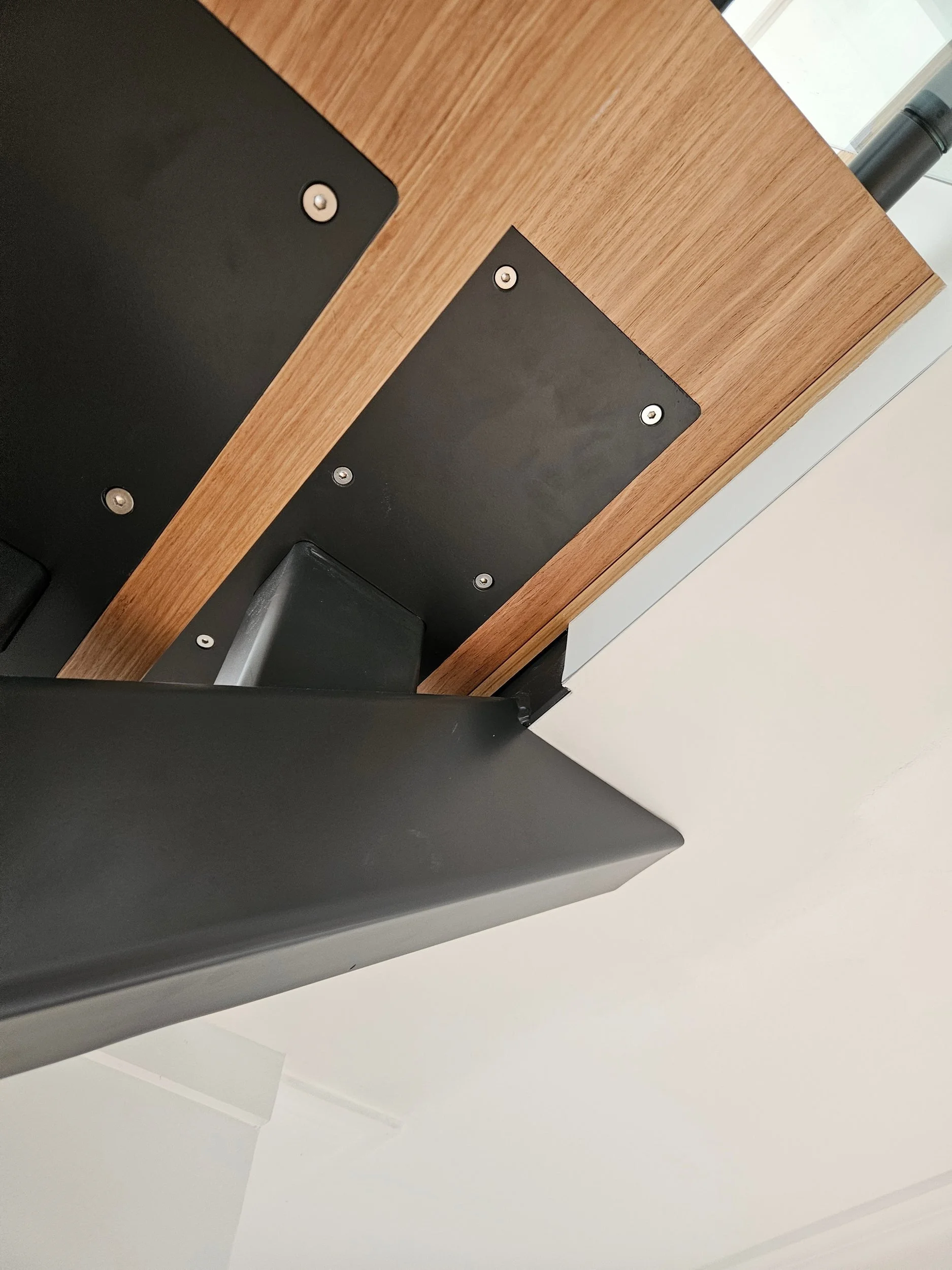 Underside of thick timber stair treads showing black steel fixing plates on a mono-stringer, Sydney