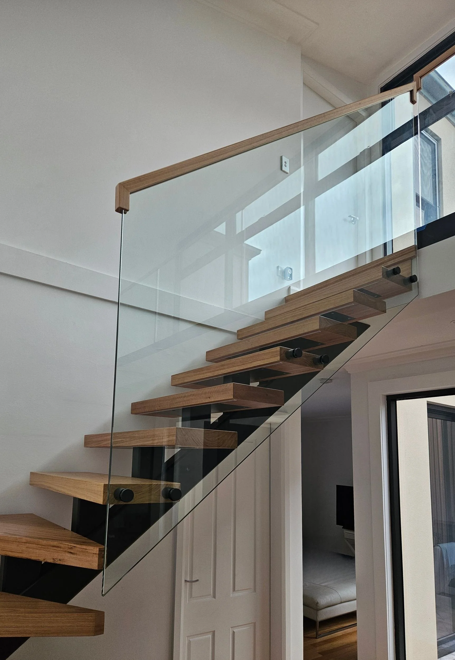Frameless glass balustrade with black standoffs and a timber handrail above timber treads on a steel mono-stringer, Sydney