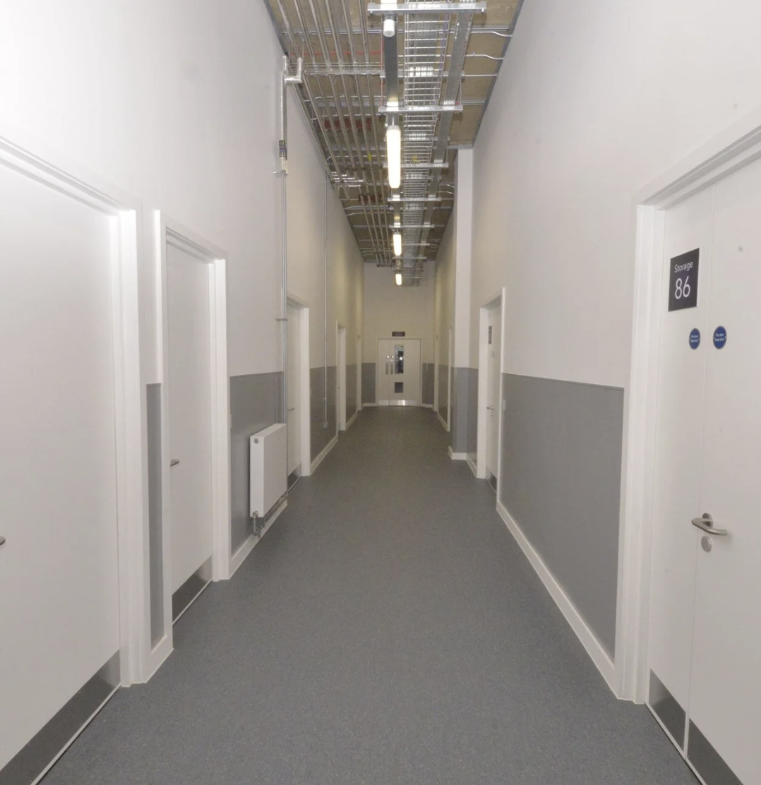Clean indoor storage facility corridor with multiple secure storage unit doors and overhead cable trays