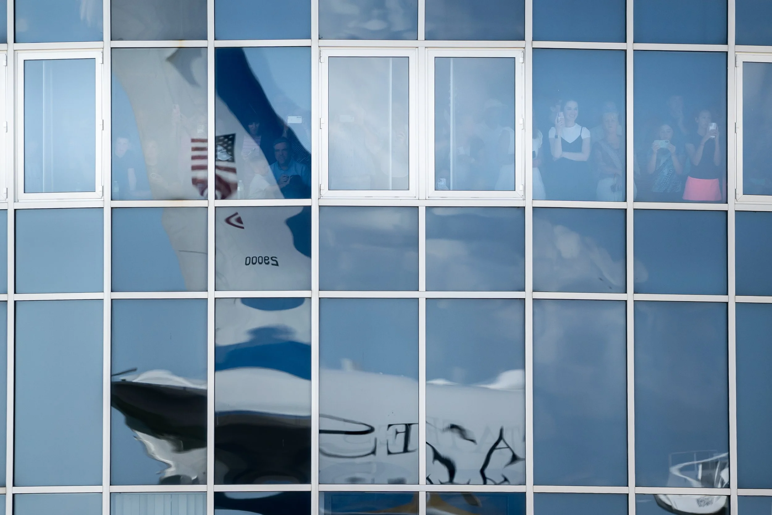  Onlookers watch as U.S. President Donald Trump arrives at Des Moines International Airport, with Air Force One reflected in the glass, in Des Moines, Iowa, U.S., July 3, 2025. 