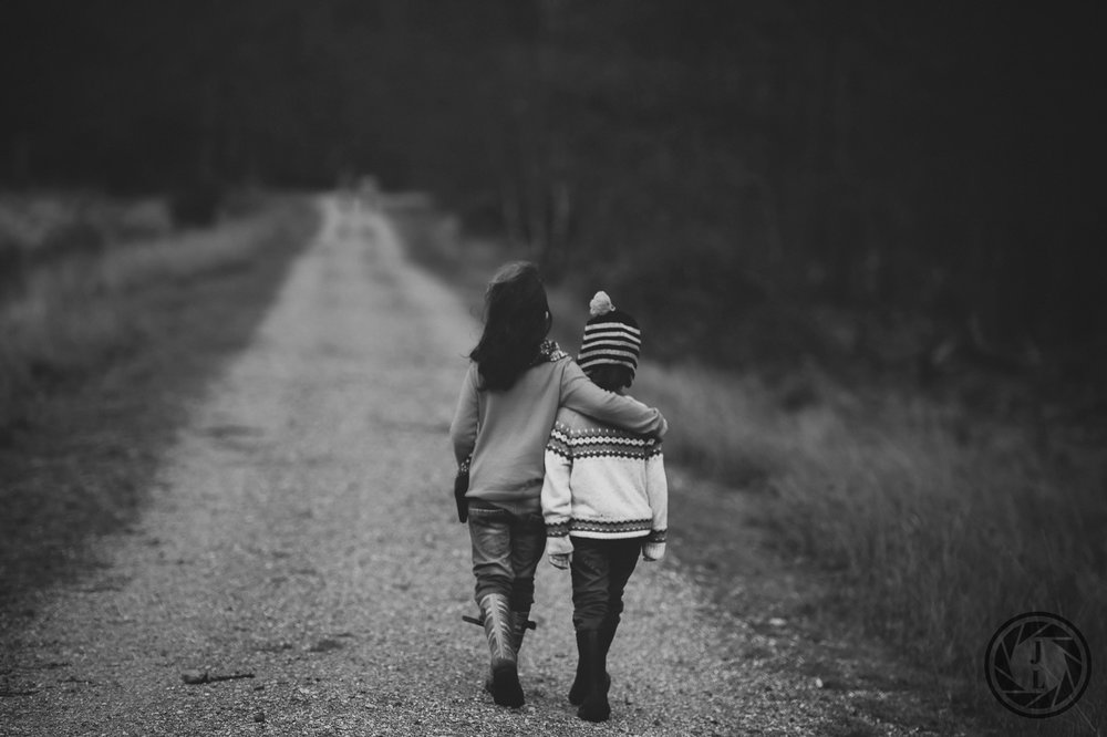  black and white image of two young kids walking arm and arm down a gravel road 