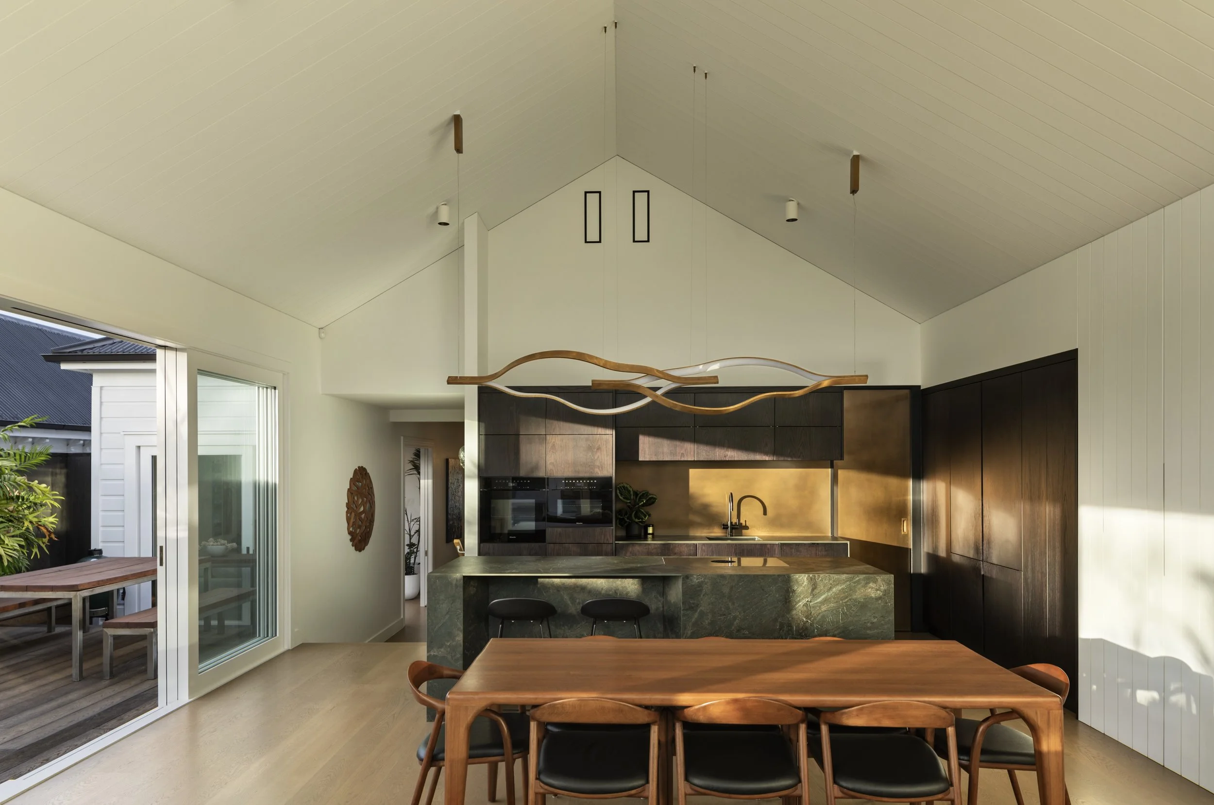 Modern kitchen and dining area with wooden dining table, black and dark wood cabinetry, and sliding glass door leading to outdoor deck.