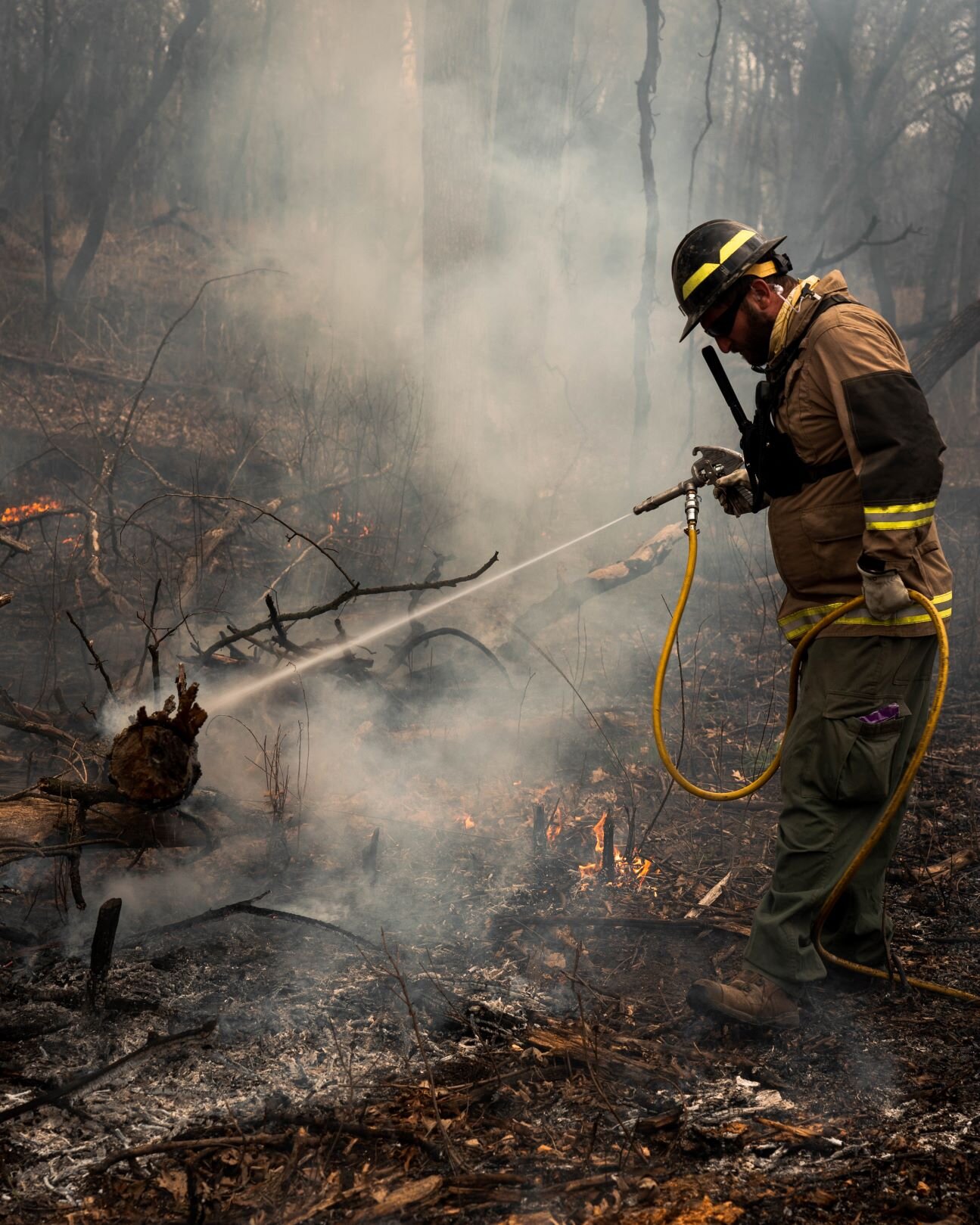 technician using a water hose to put out a burning log